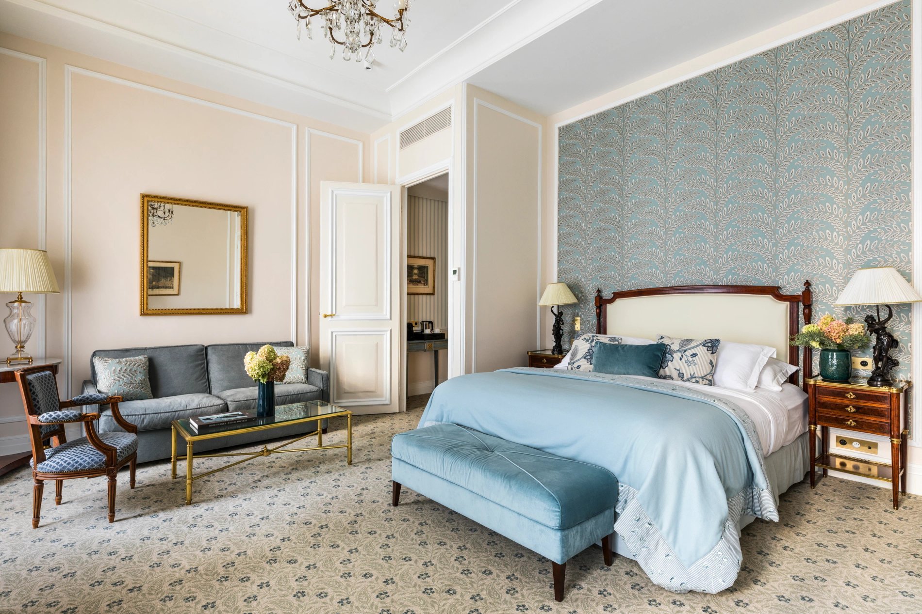 Vue d’ensemble d’une Junior Suite à l’Hôtel San Régis Paris, lit double, salon chic et murs aux tons bleus.