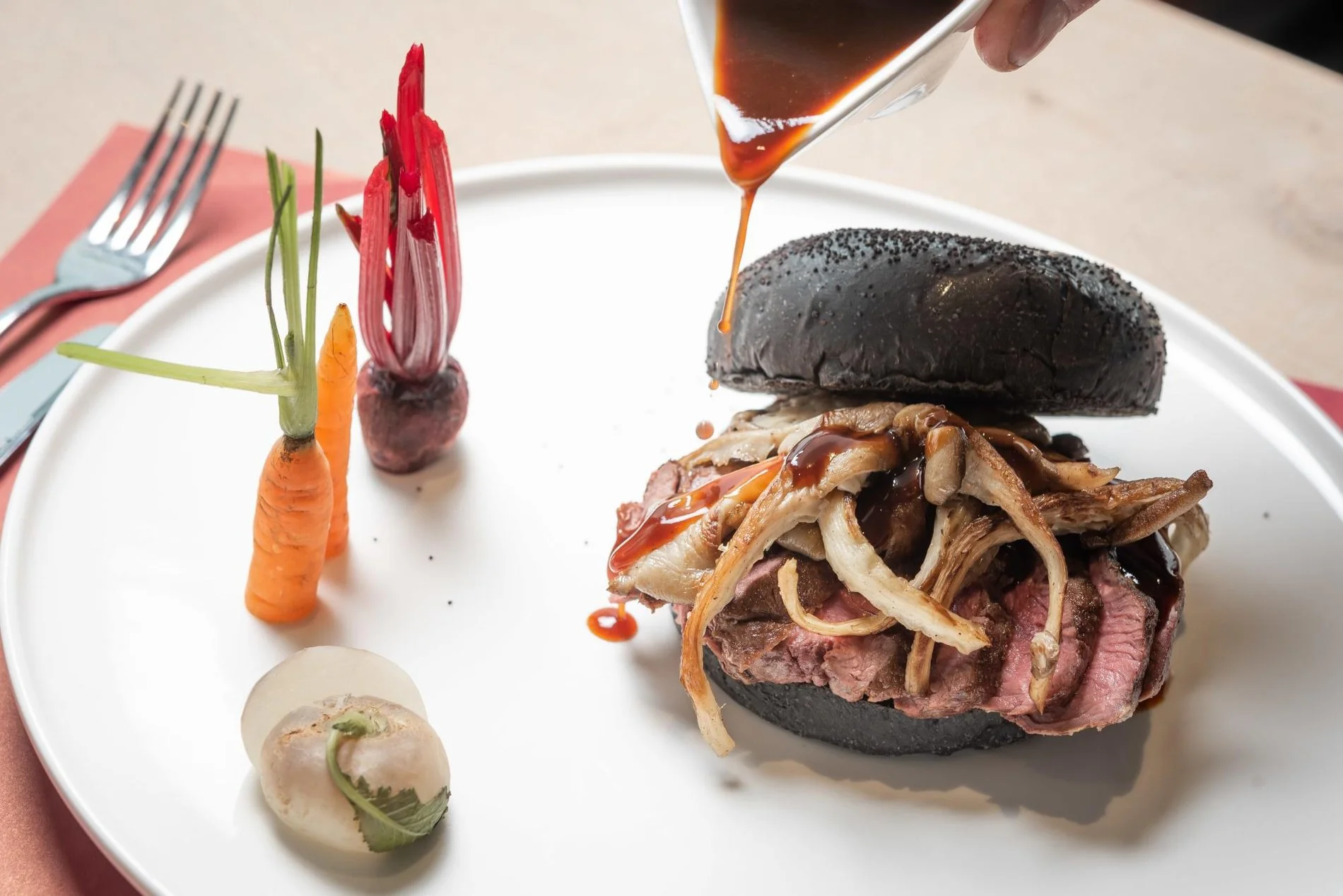 Black bun burger with garnish, served with fries and condiments, presented on a table.