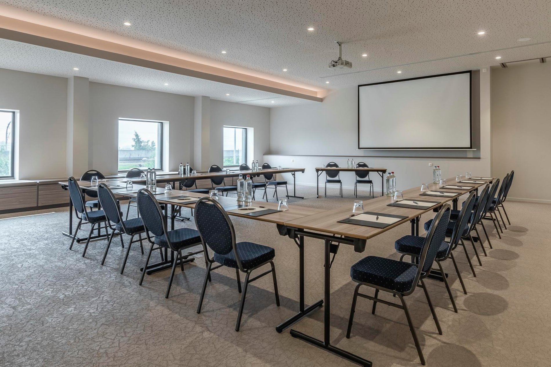 Heldere vergaderzaal met tafels, stoelen en een projectiescherm.