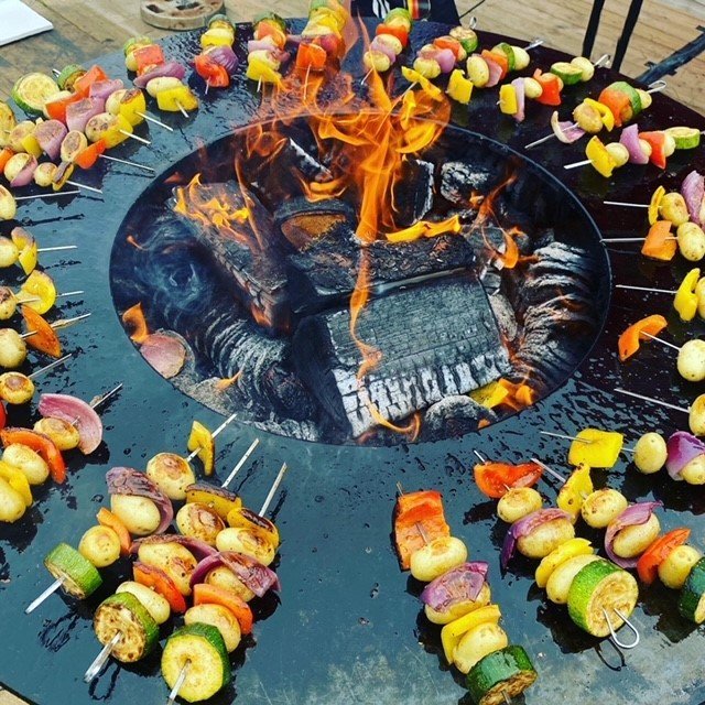 Circular barbecue with colorful skewers and flames in the center for communal cooking.