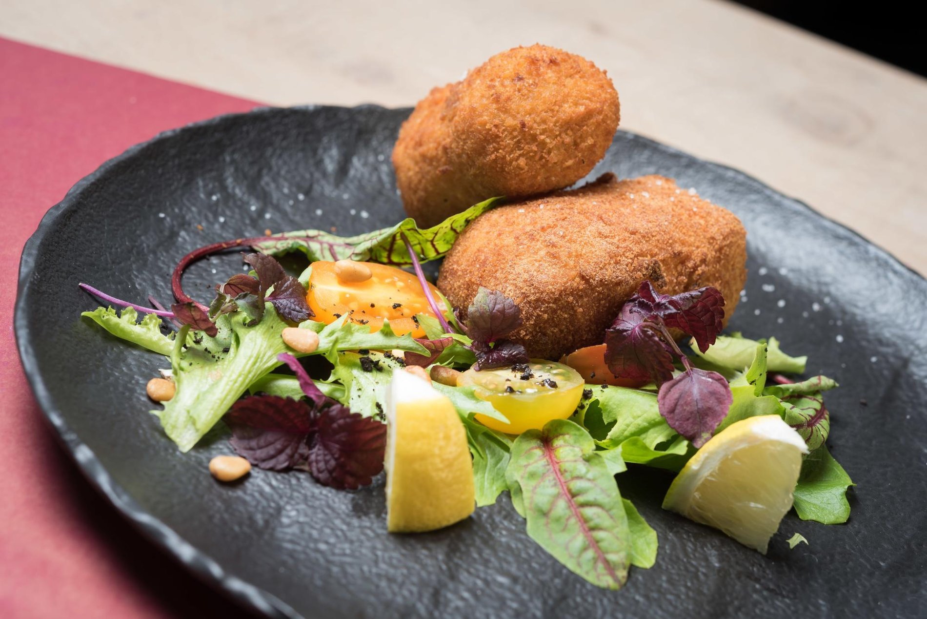 Crispy croquettes served on a bed of fresh salad with sides.