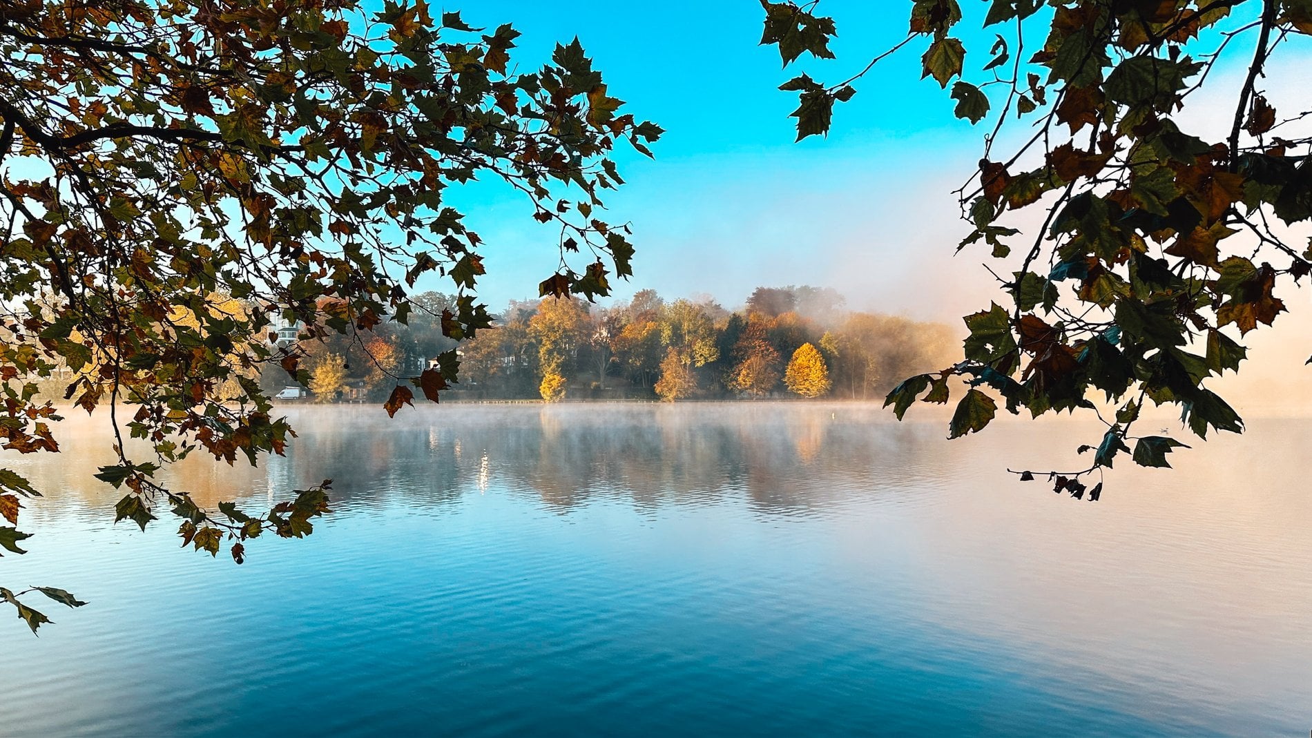 Panoramablick auf Martin's Château du Lac vom See aus, umgeben von Bäumen und einem bewölkten Himmel.