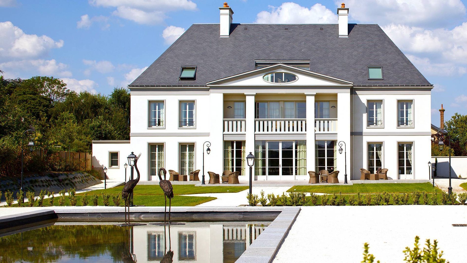 Façade principale de l'Hôtel La Ramade avec bassin d'eau en façade, symbolisant l'élégance architecturale et les aménagements paysagers.