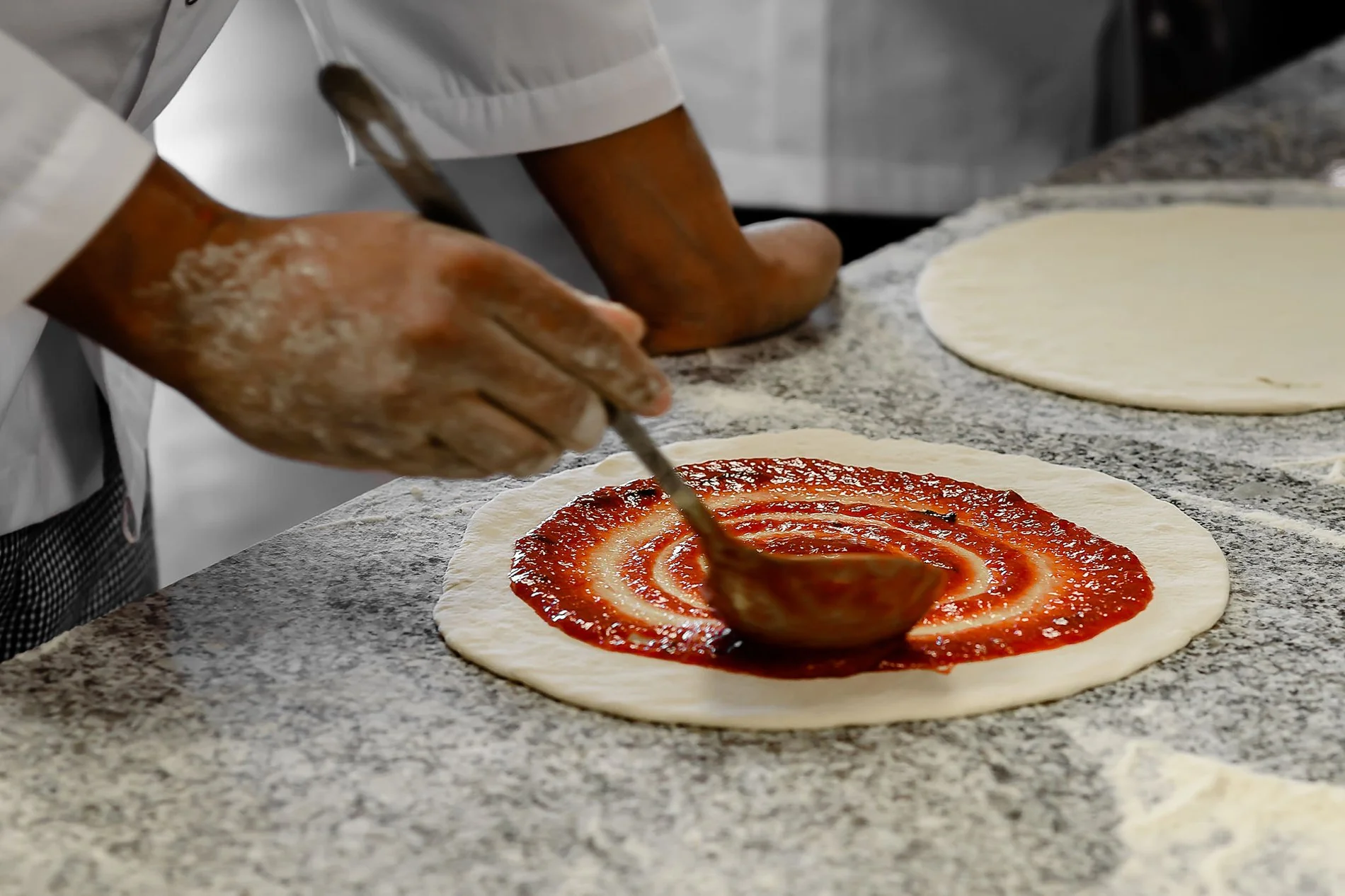 Chef versant la sauce tomate sur la base de la pizza au restaurant Al Italiu de l’Hôtel Jupiter Albufeira
