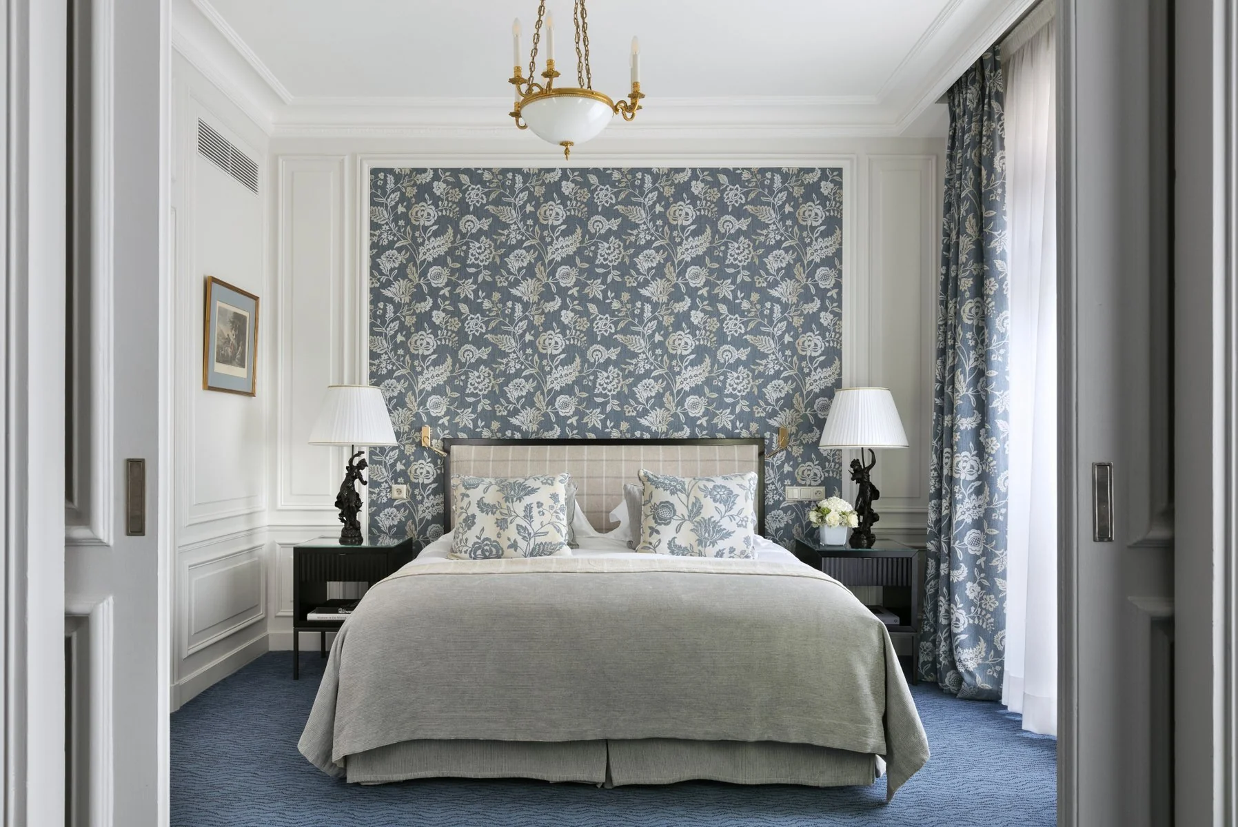 Chambre Junior Suite lumineuse à l’Hôtel San Régis Paris 8, mur floral bleu et ambiance sereine.