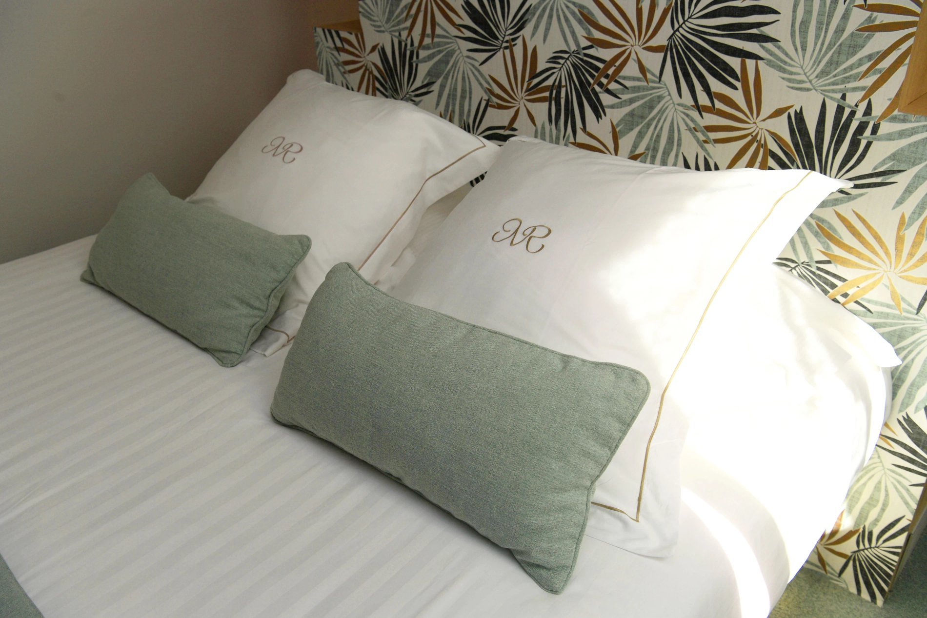 Standard room bed at Hotel La Ramade with green pillows, symbolizing comfort and a cozy ambiance.