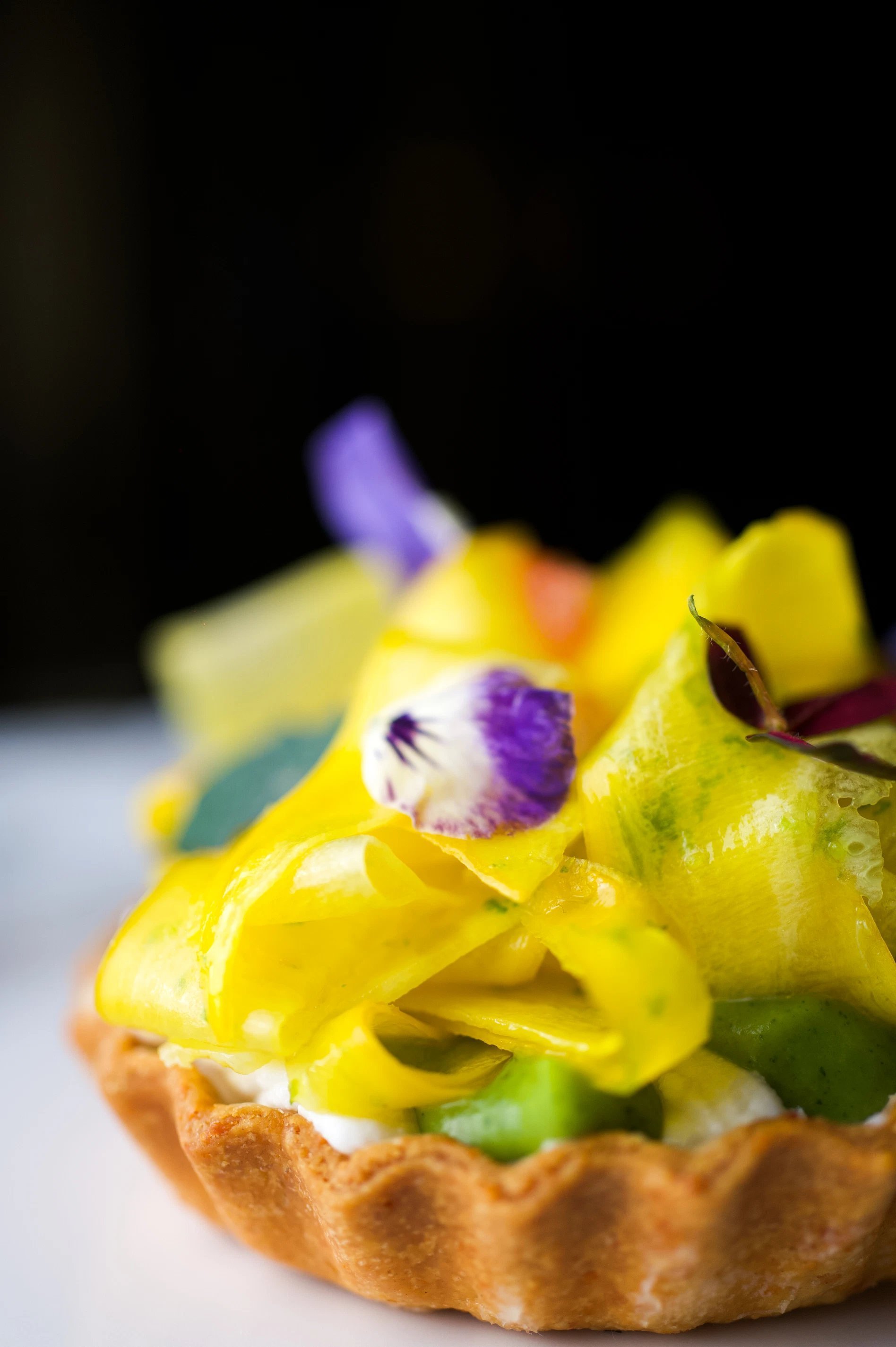 Gros plan sur une tartelette colorée aux légumes et fleurs comestibles, servie à l’Hôtel San Régis.