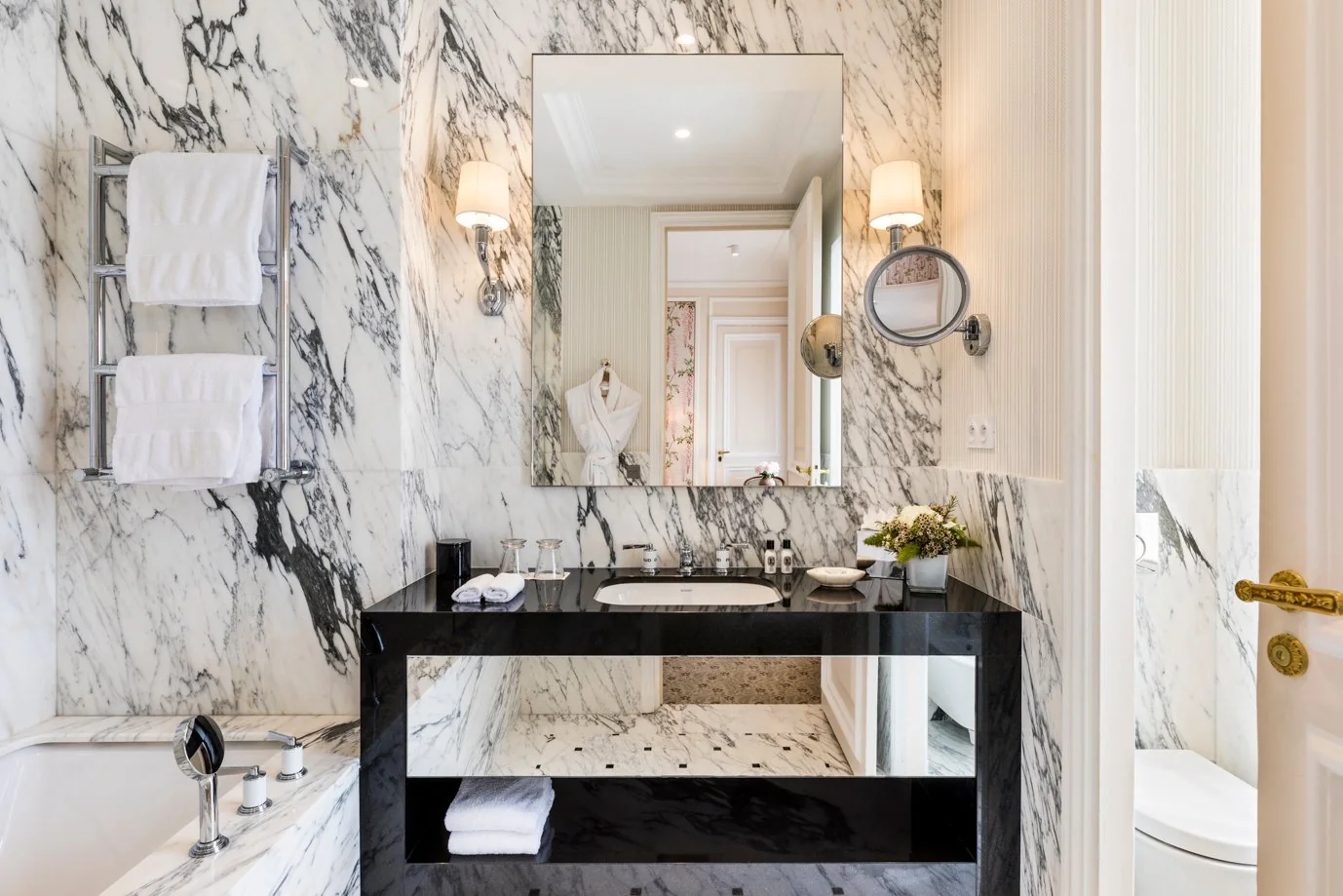 Salle de bain en marbre blanc et noir de l’Hôtel San Régis à Paris, avec baignoire, vasque design et lumière naturelle.