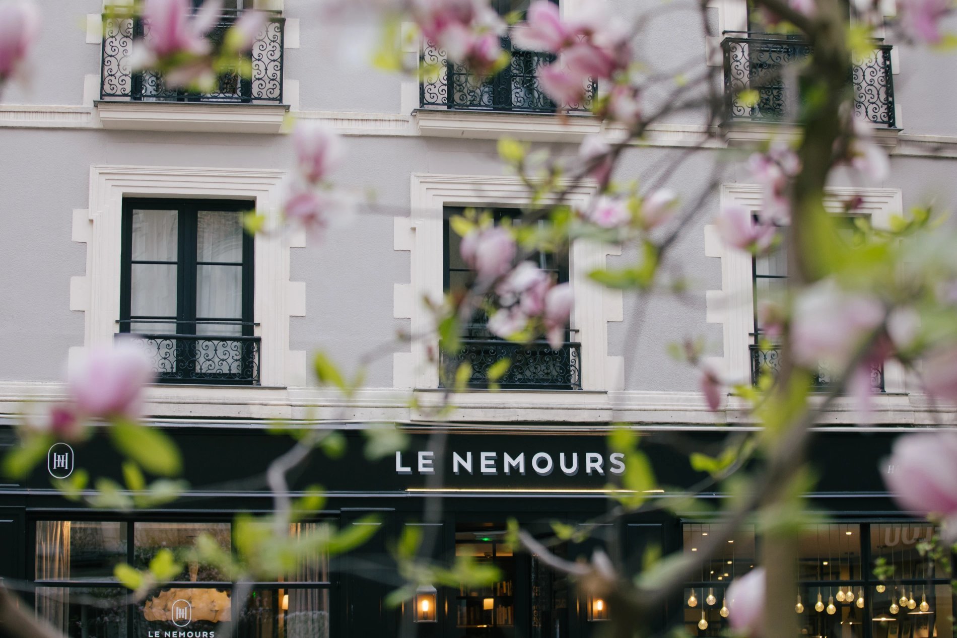 Façade de l'hôtel Le Nemours Hôtel & Appartements à Rennes, entourée de fleurs printanières.