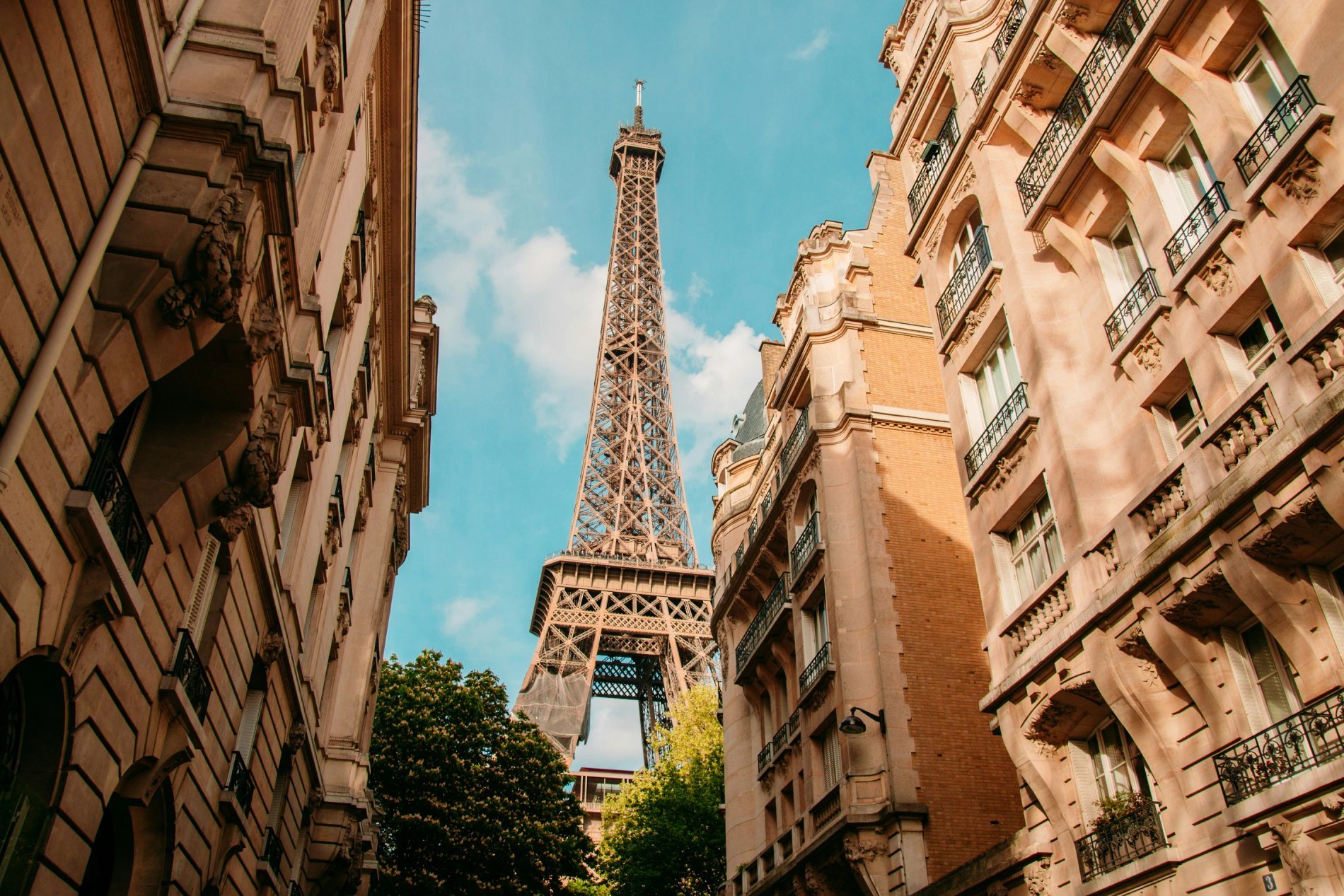 Eiffel Tower with a vast blue sky and beautiful Haussmann buildings, viewed in low angle from a street near Bir-Hakeim.