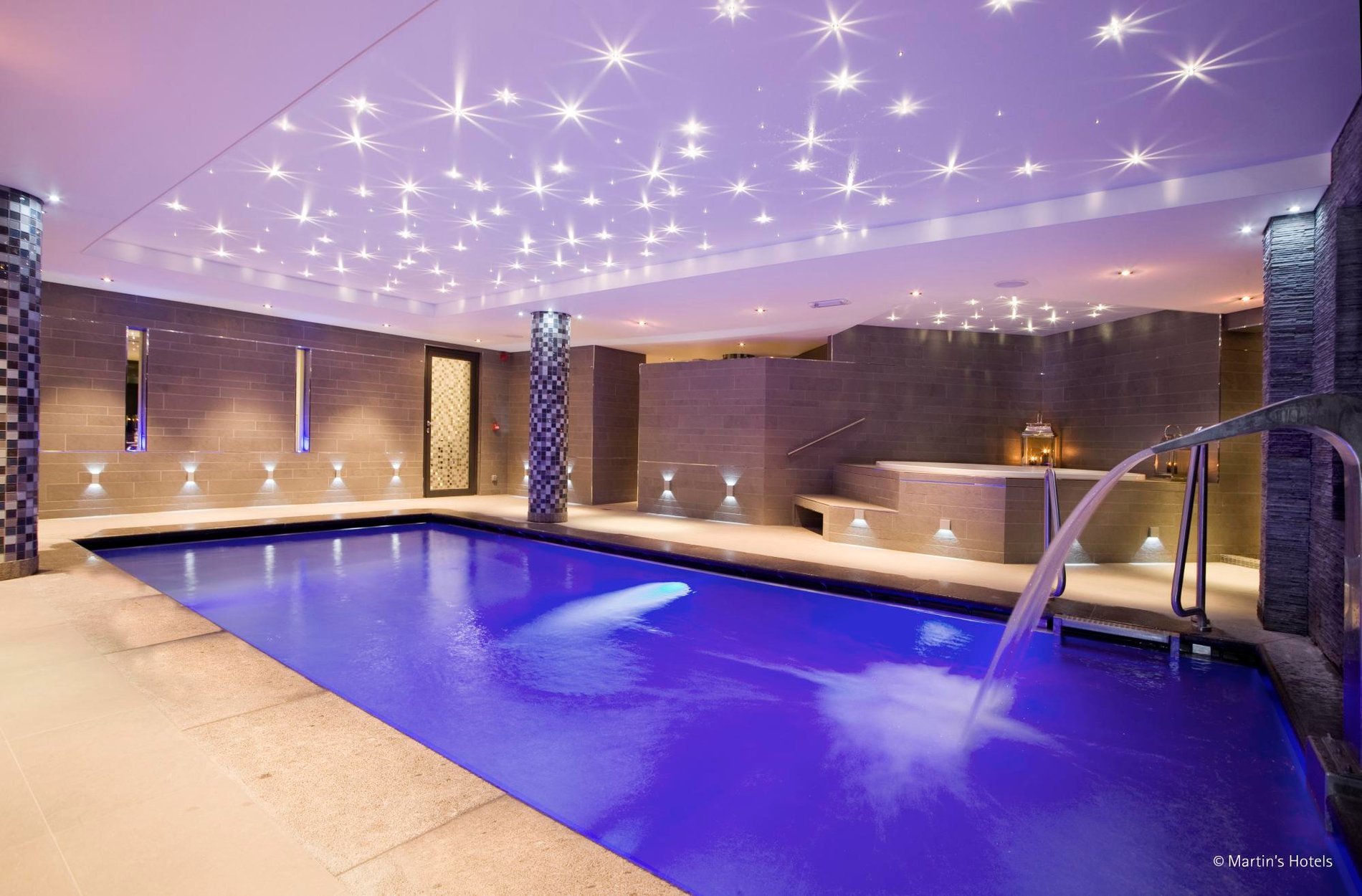 Illuminated indoor pool with waterfall at Martin's Château du Lac hotel.