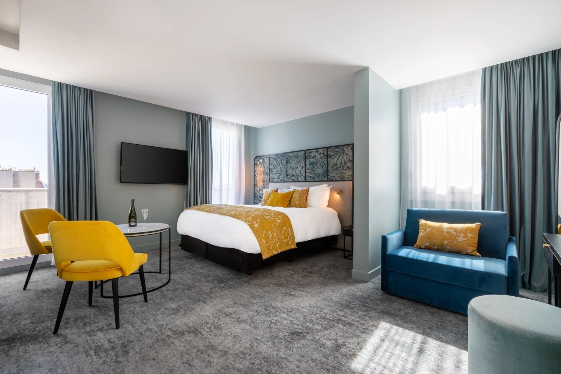 Comfortable Premium Room at VOCO Paris Montparnasse with a double bed, a yellow armchair, and a blue sofa.