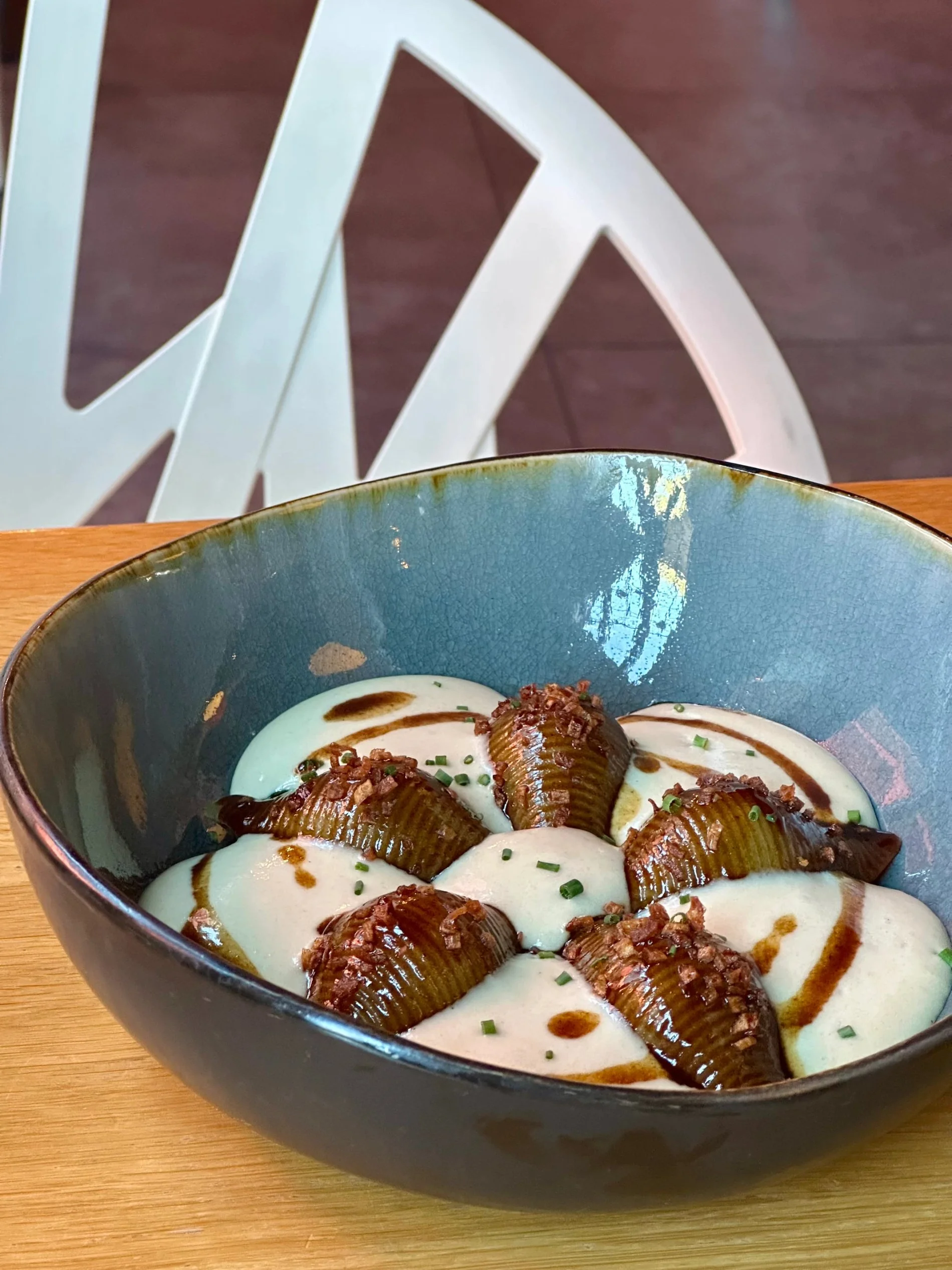 Plat gastronomique servi dans un bol en céramique avec une sauce crémeuse et des herbes.