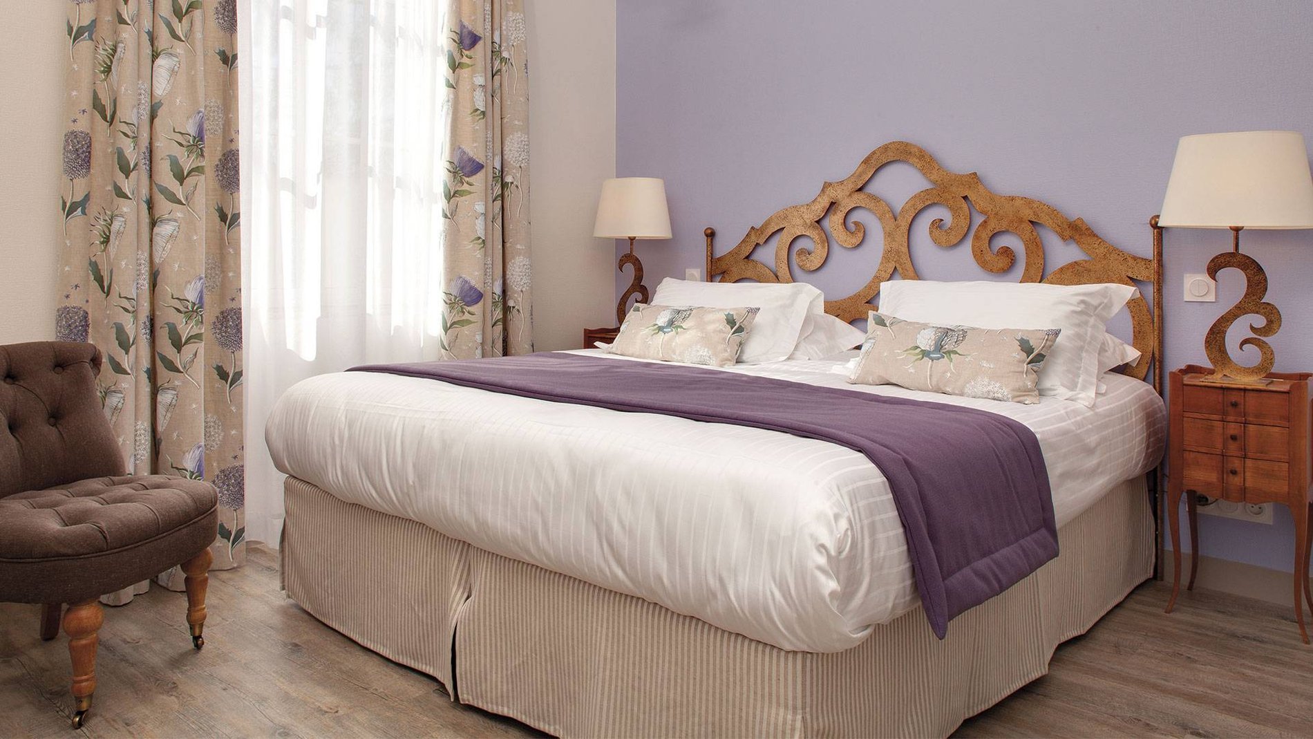 Chambre Standard de l'Hôtel La Ramade avec literie violette et tête de lit en bois, symbolisant un espace confortable et classique.