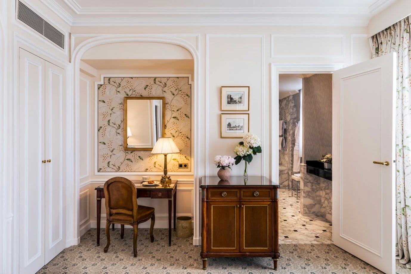 Vue d’une suite de l’Hôtel San Régis à Paris, avec coin bureau raffiné, mobilier ancien et accès à une salle de bain en marbre.