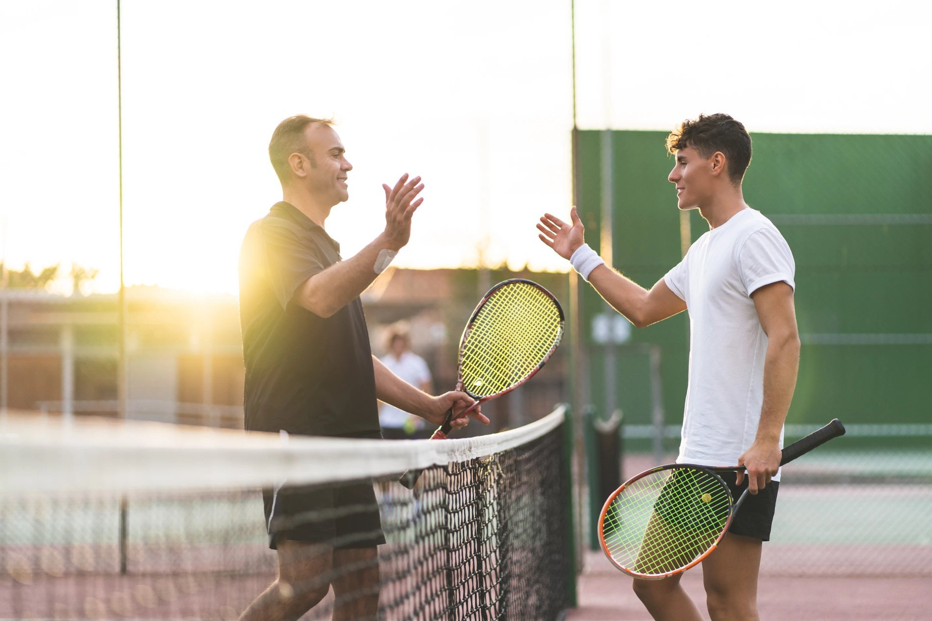 Twee spelers die elkaar begroeten met hun rackets op een outdoor padelbaan.