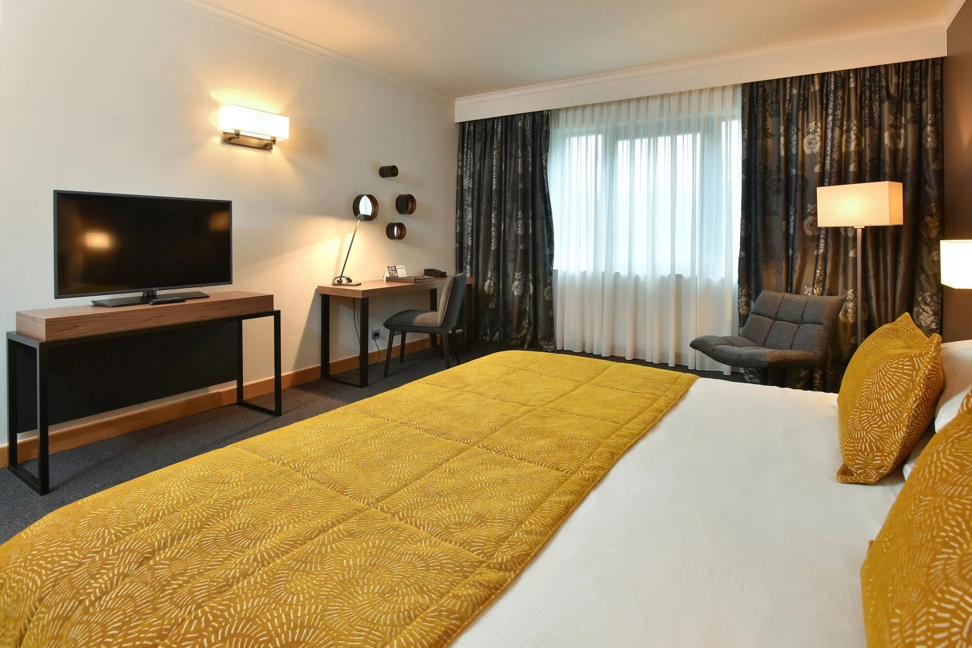 Ruime kamer met tweepersoonsbed, gele sprei en bureauhoek bij Martin's Château du Lac.