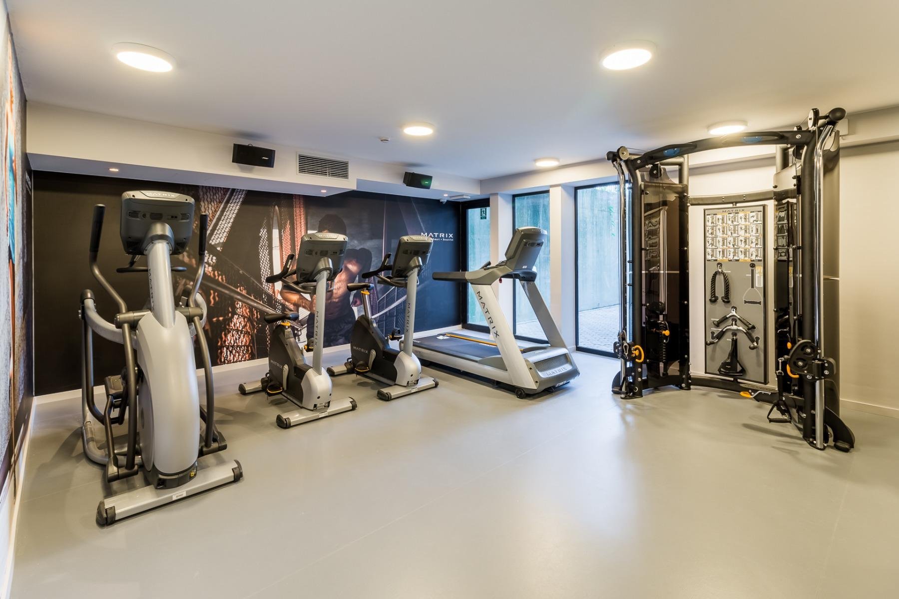 Ruime fitnessruimte met krachttoestellen, cardiotoestellen en halters in een moderne omgeving.