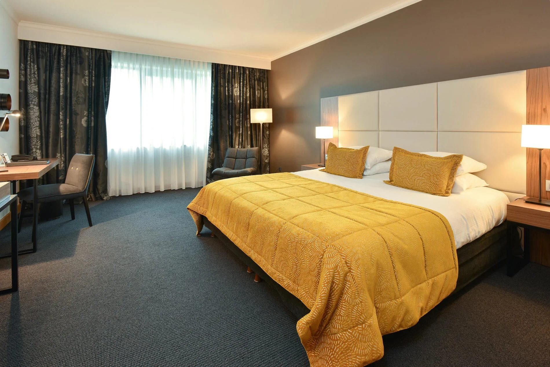 Chambre moderne avec lit double, couvre-lit jaune et large fenêtre.