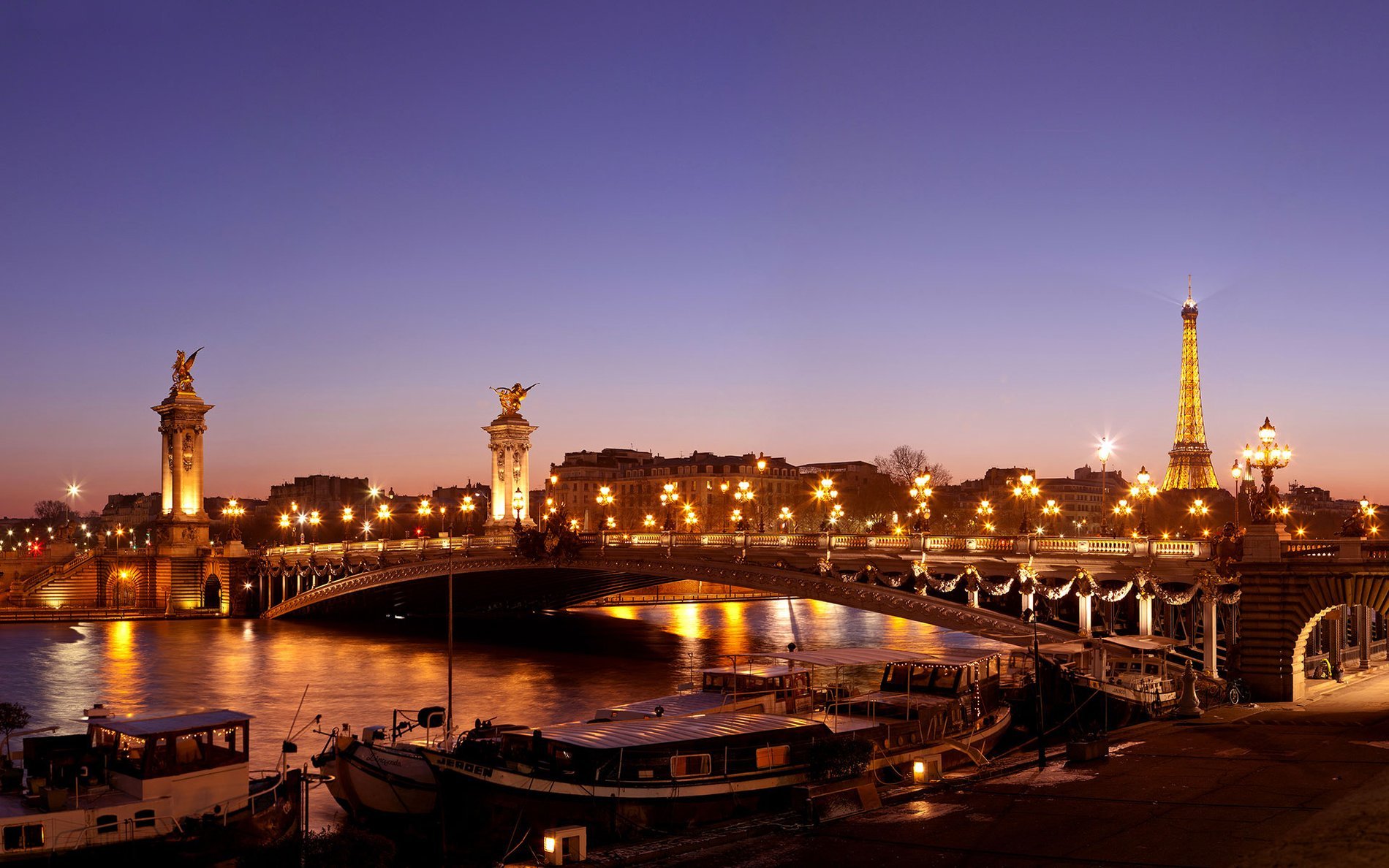 The Alexandre III Bridge lit up at dusk with the Eiffel Tower in the background, just steps from Hôtel San Régis, perfect for a romantic Paris getaway.