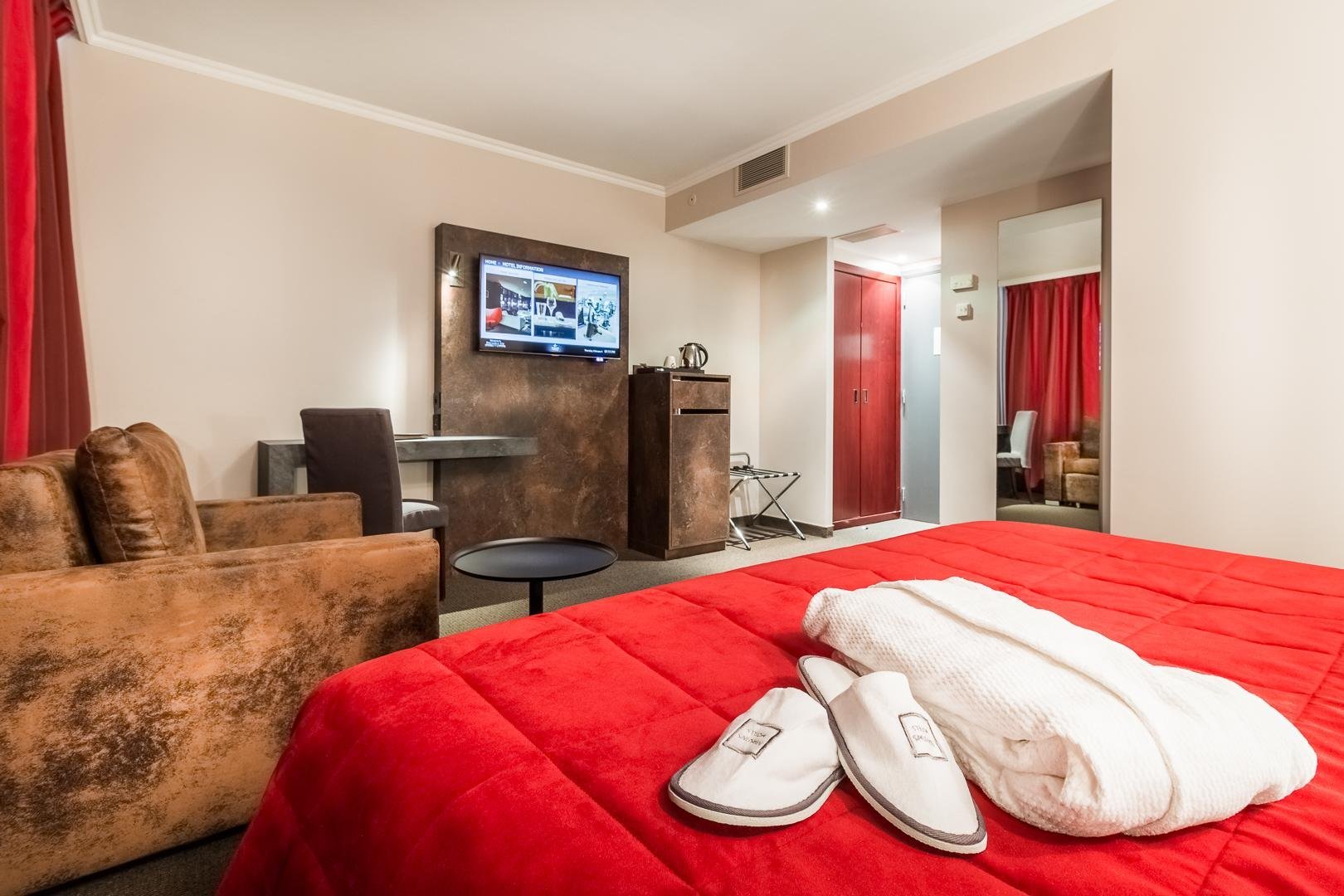 Spacious room with a red bed and sitting area, robes provided