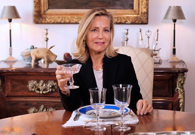 Portrait d'une femme élégante tenant un verre à pied à table, dans un intérieur classique de l'Hôtel San Régis