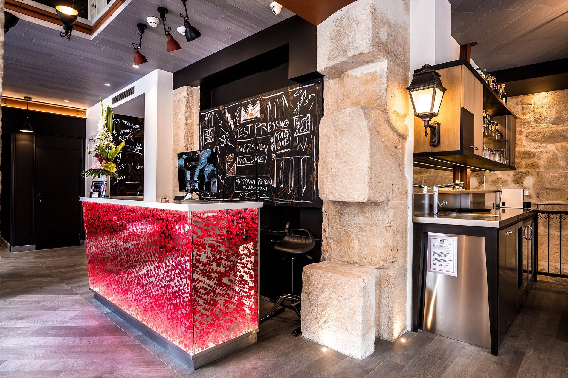 Entrance and reception area of the Marais Grands Boulevards Hotel in Paris, featuring a luminous counter and exposed stone walls.