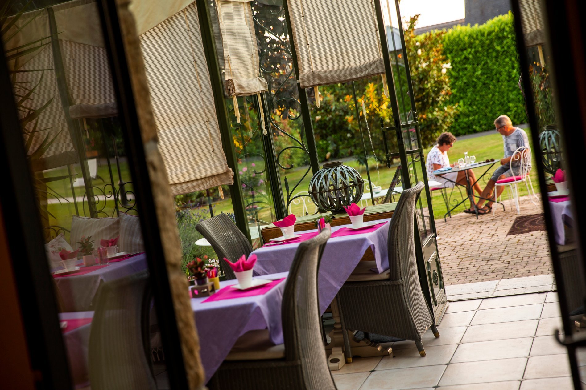 Vue partielle de la véranda de l'Hôtel La Ramade avec tables et chaises, symbolisant l'aménagement pour le petit-déjeuner ou des événements.