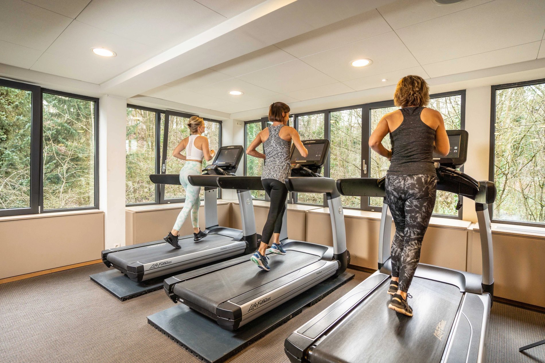 Moderner Fitnessraum mit Laufbändern und großen, hellen Fenstern.