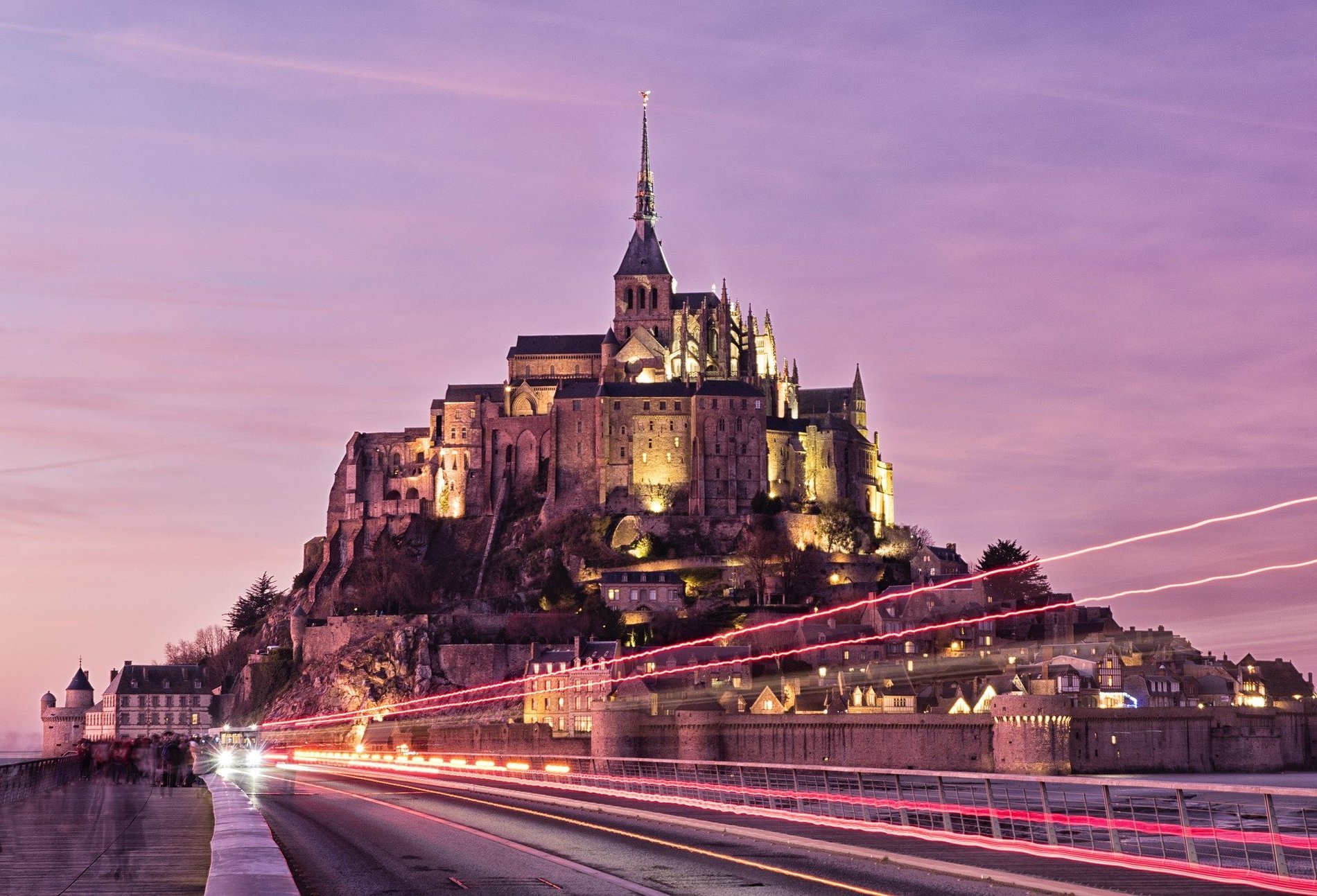 Mont Saint-Michel illuminated at night, with light trails from cars, symbolizing the magic of the site in the evening.