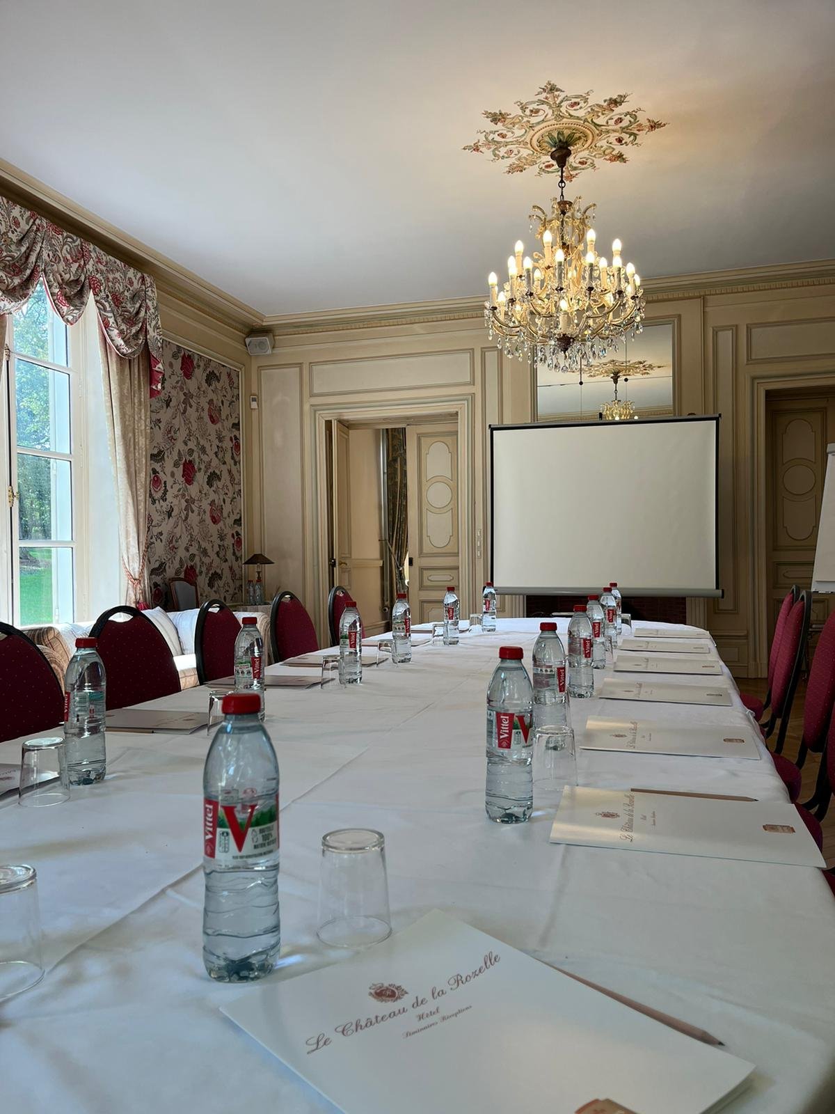 Château de la Rozelle, Salle de réunion élégante avec une grande table, des chaises rouges et un projecteur.