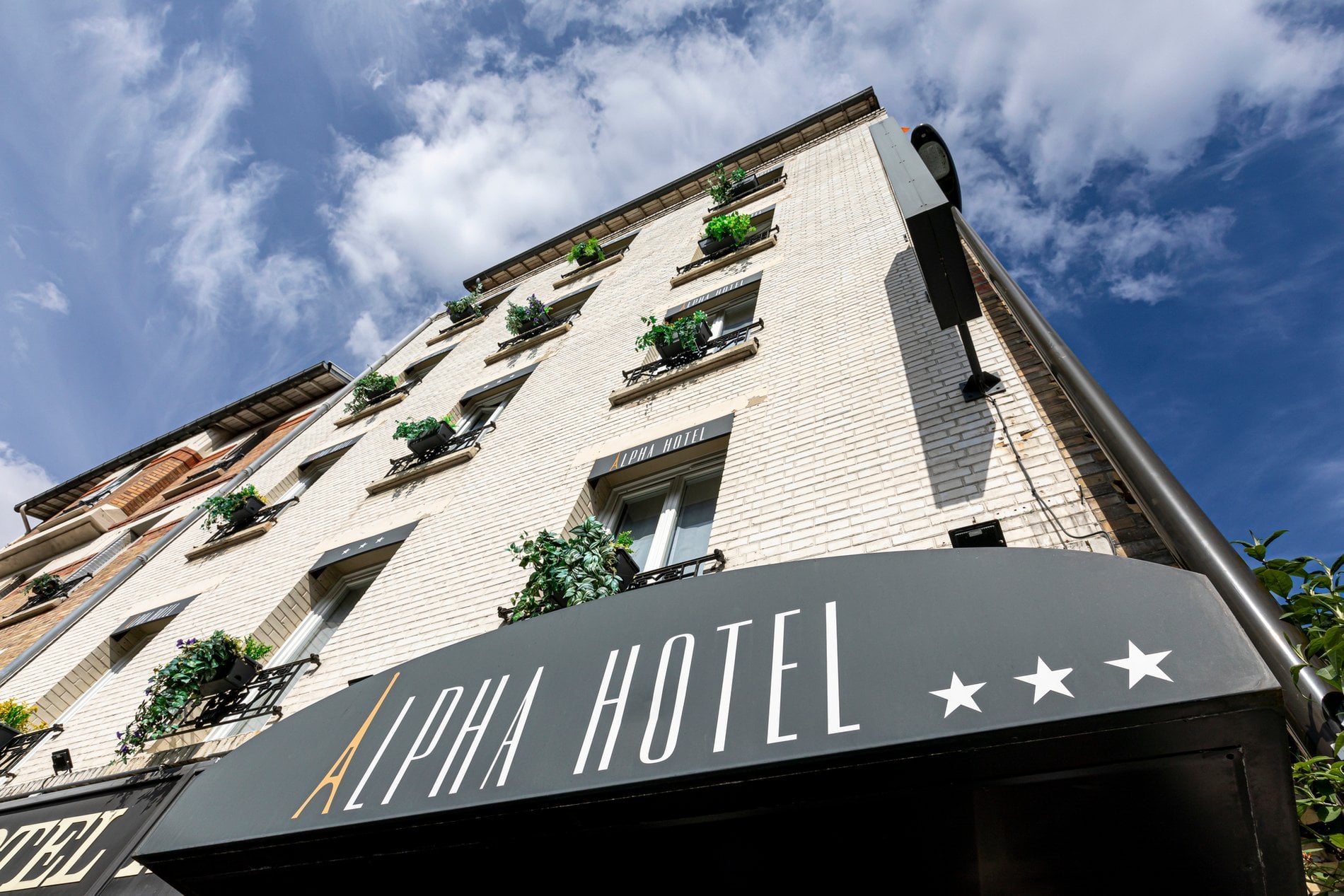 Façade de l'Hôtel Alpha Paris Eiffel à Boulogne-Billancourt avec enseigne et fenêtres fleuries.