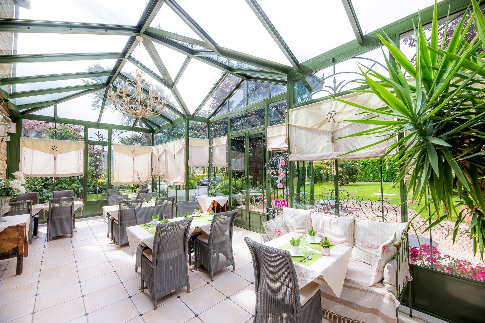 Intérieur de la véranda de l'Hôtel La Ramade avec tables dressées, symbolisant un espace spacieux et lumineux pour les repas.