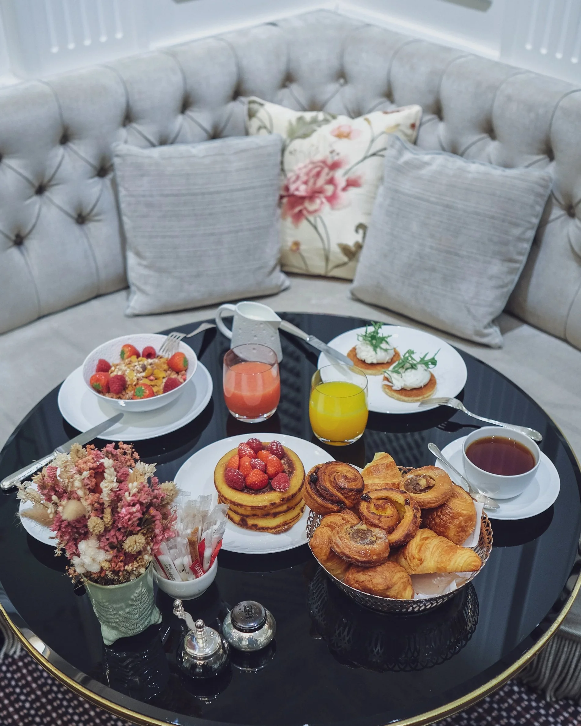 Sélection gourmande pour le tea time à l’Hôtel San Régis, servie sur banquette fleurie avec viennoiseries, jus et fruits.