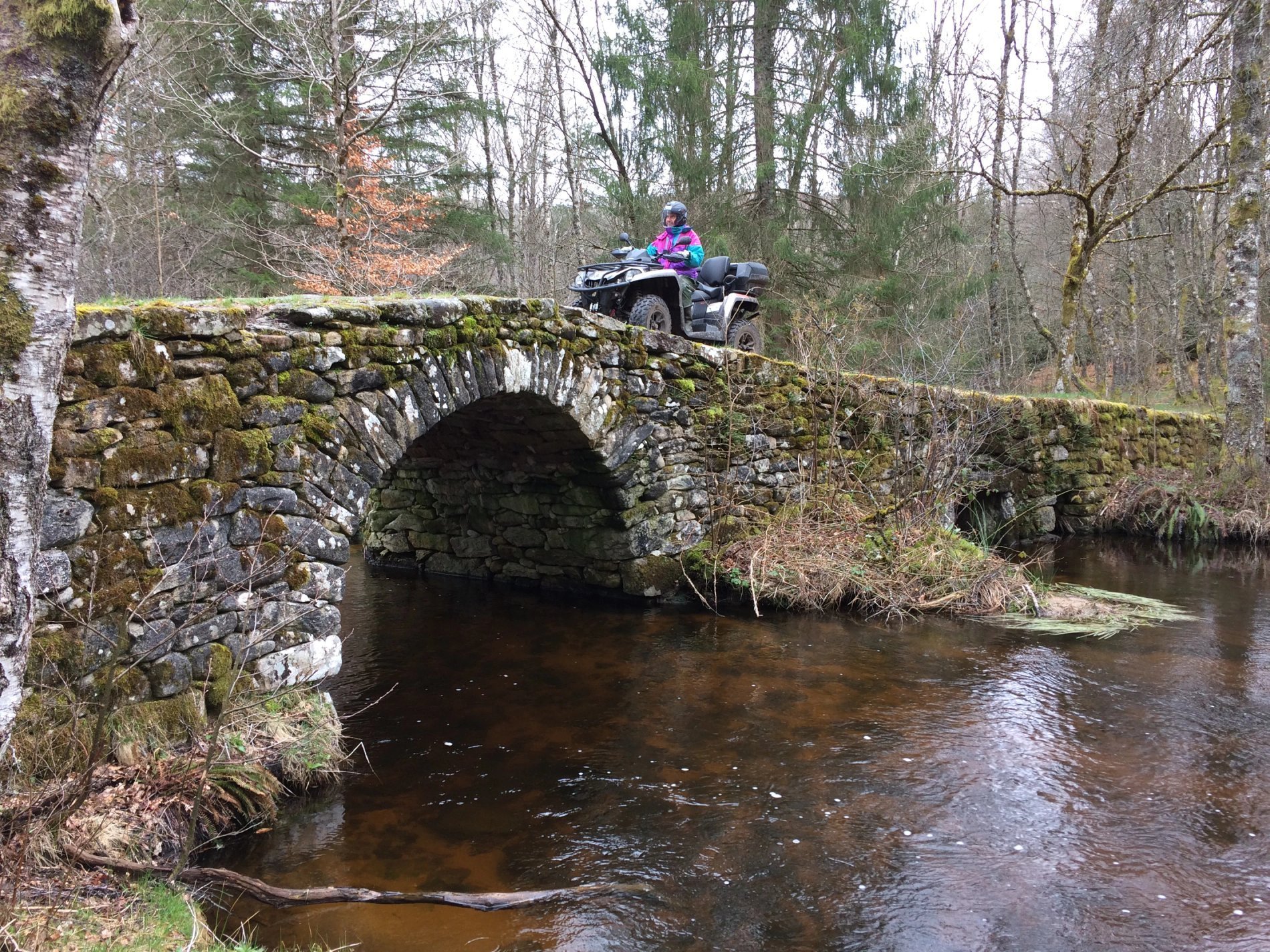 Pont en pierre sur une rivière, traversé par un quad en forêt, activité encadrée par Villa Corrèze Aventure.