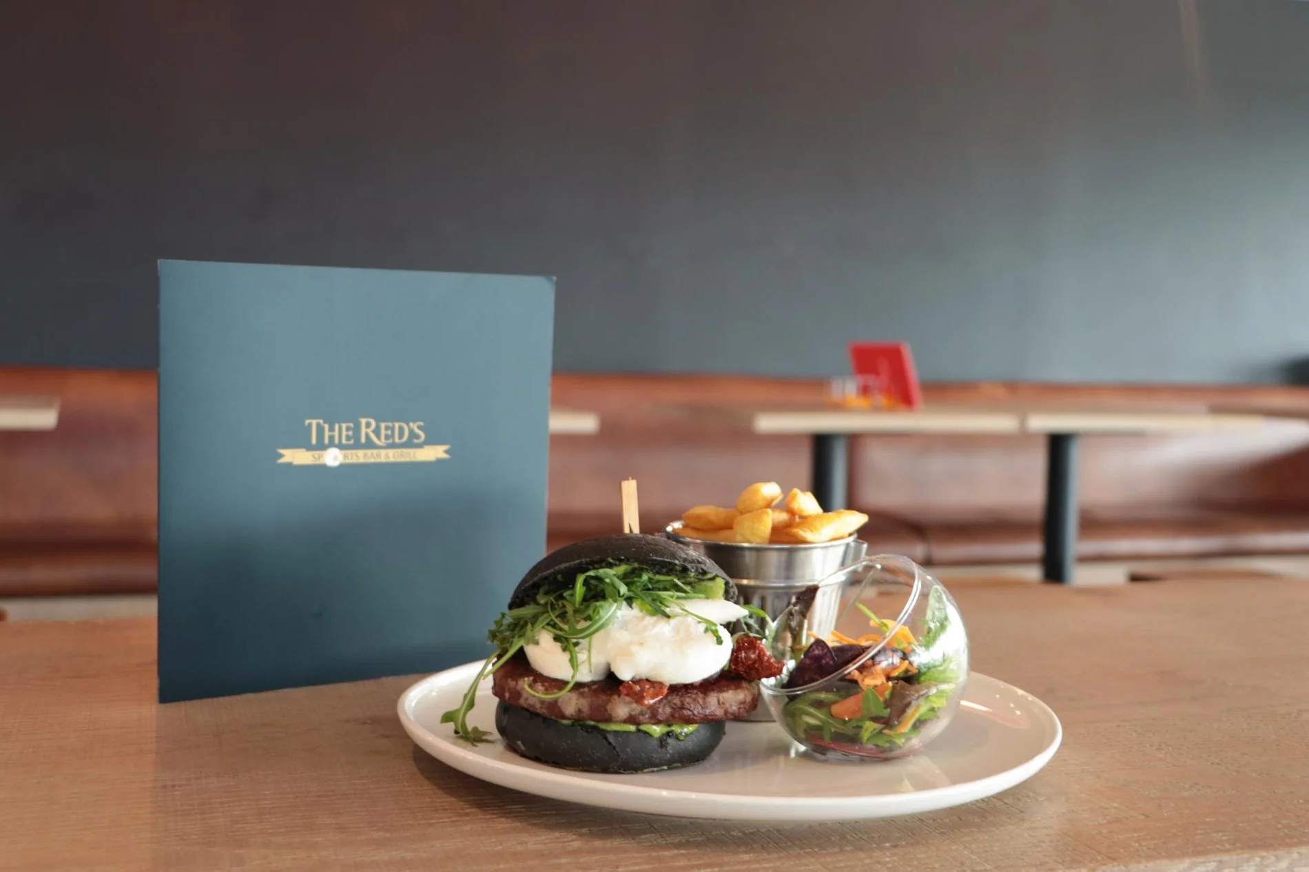 Two elegantly plated dishes and a blue menu card from The Red's restaurant on a wooden table.