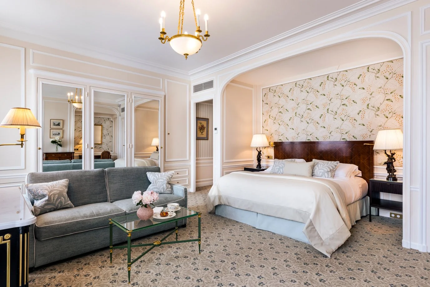 Suite lumineuse de l’Hôtel San Régis à Paris, avec lit king-size, salon élégant et décoration florale murale raffinée.
