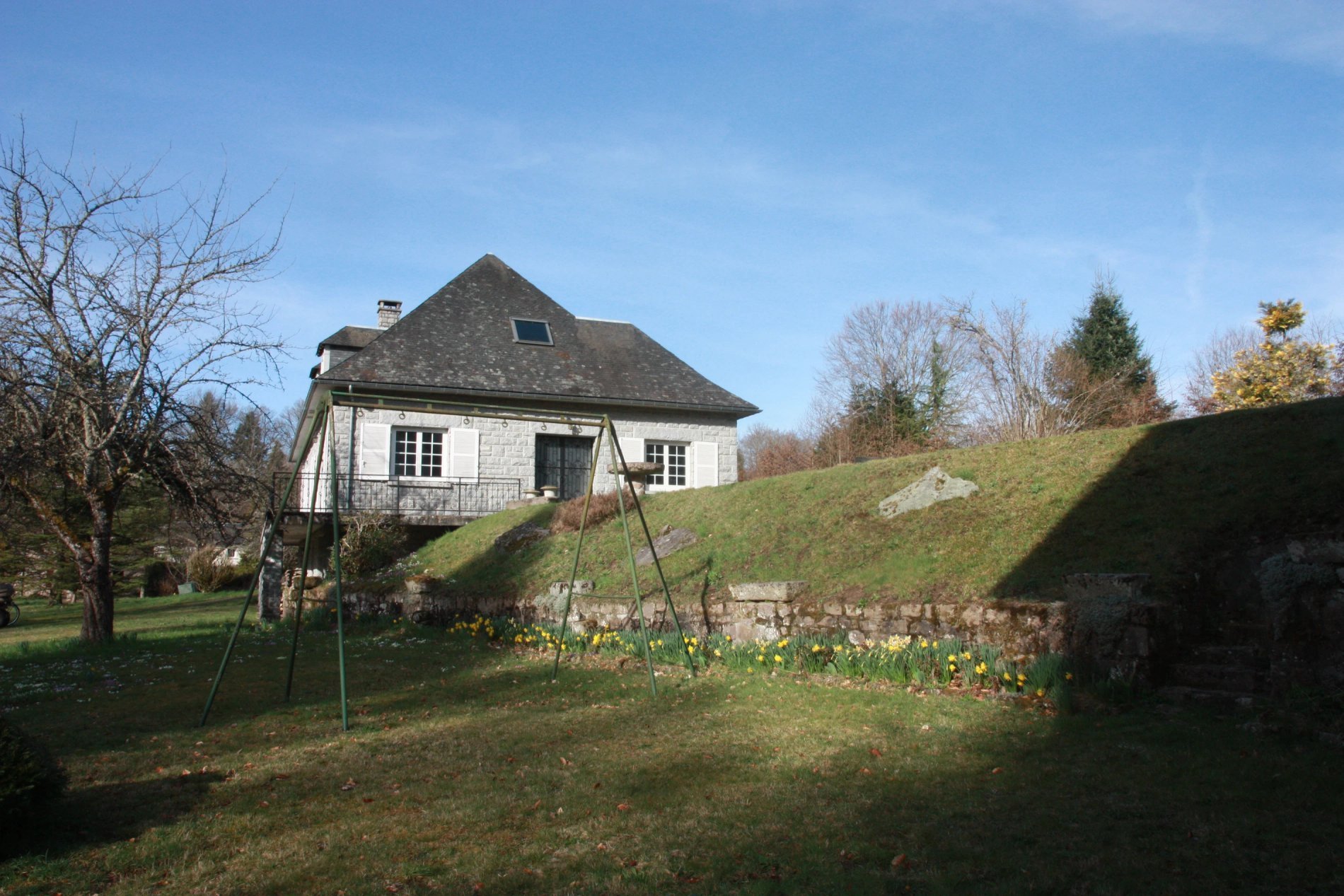 Extérieur de Villa Corrèze Aventure avec portique de balançoire, pelouse en pente et maison en arrière-plan.