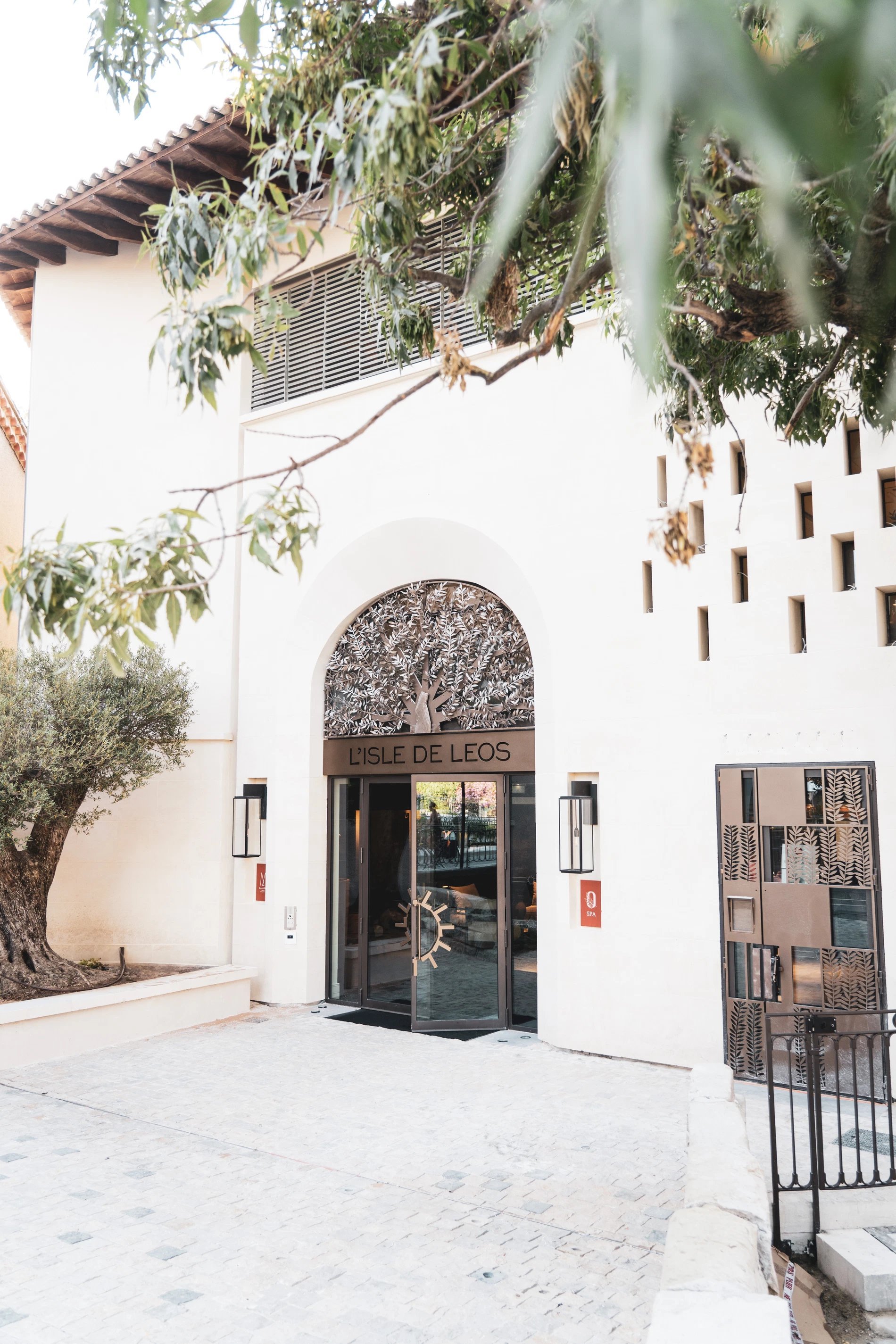 Façade principale de L’Isle de Leos avec arche en fer forgé et oliviers aux alentours.