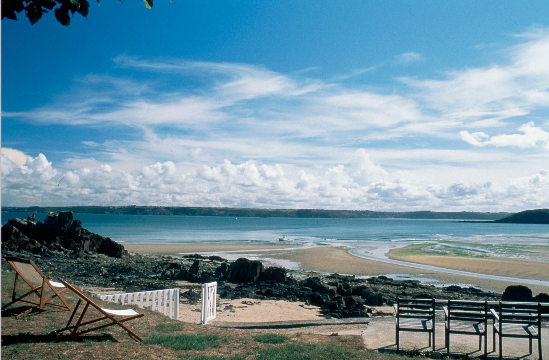 Vue sur une plage avec des chaises longues et des bancs sous un ciel bleu