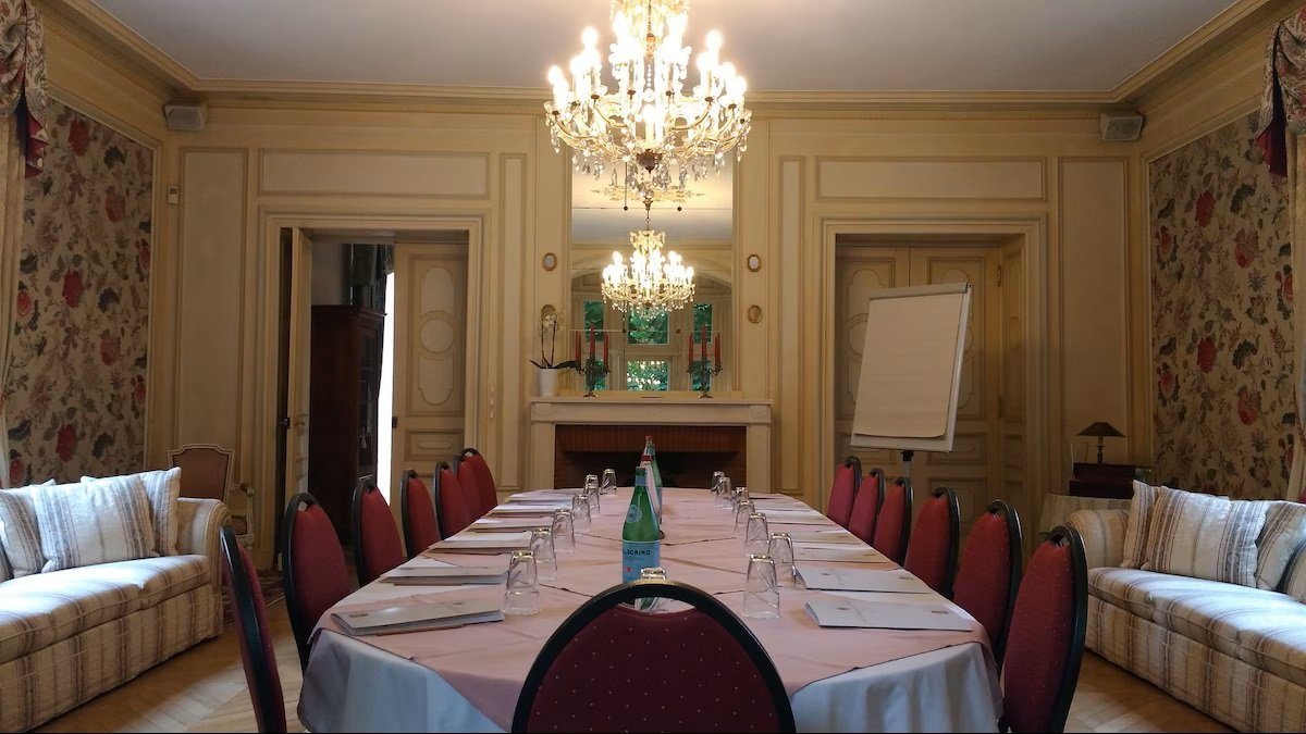 Salle de réunion élégante avec une grande table entourée de chaises, décorée avec des lustres et des canapés.