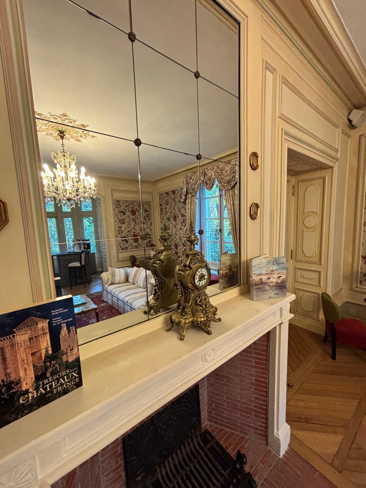 Château de la Rozelle, Intérieur d'un salon avec un miroir, une horloge ancienne et un lustre.