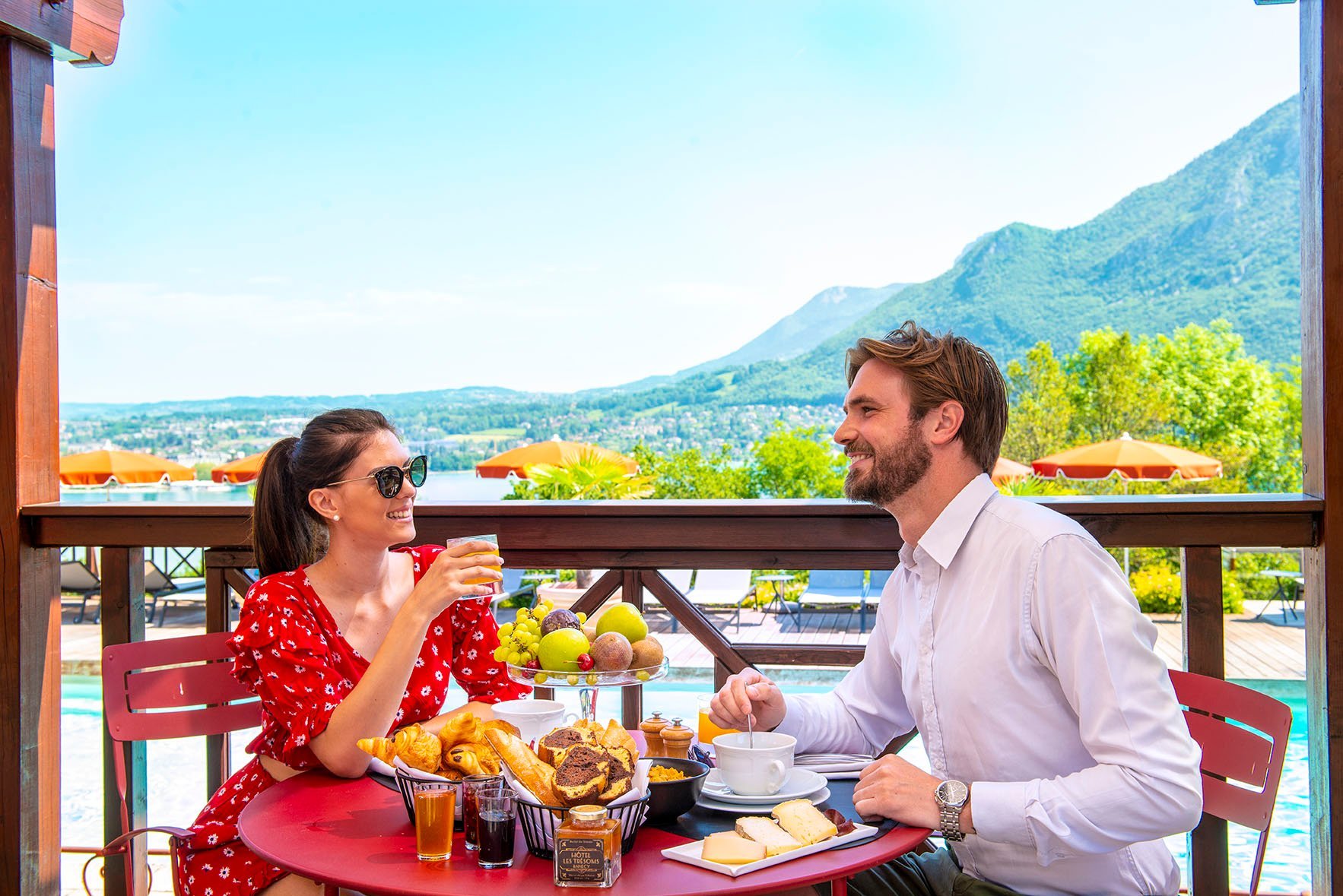 Couple dégustant un petit déjeuner sur leur terrasse extérieur avec une vue imprenable sur le lac d'Annecy et les montagnes de Haute Savoie