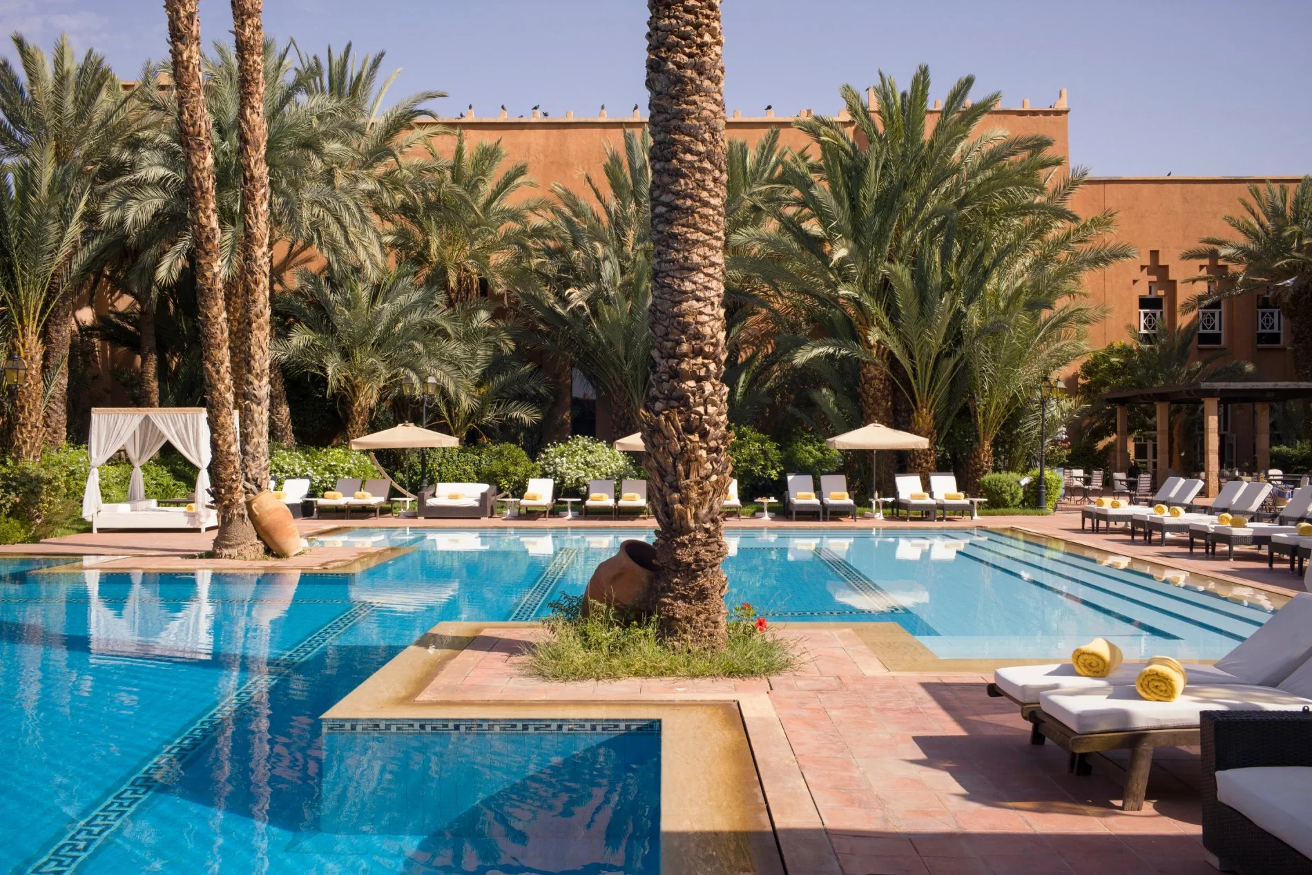 Piscine entourée de palmiers et transats au Berbère Palace à Ouarzazate