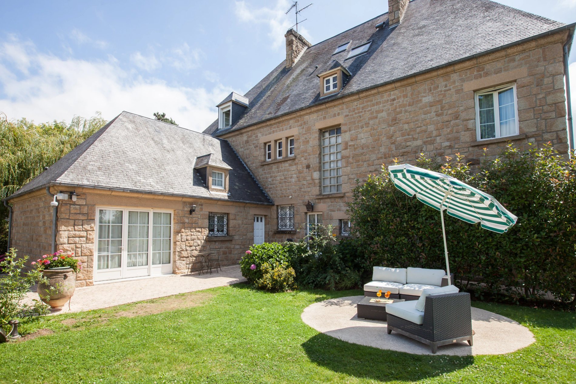Façade arrière de l'Hôtel La Ramade avec coin salon extérieur et parasol, symbolisant un espace de détente privé.