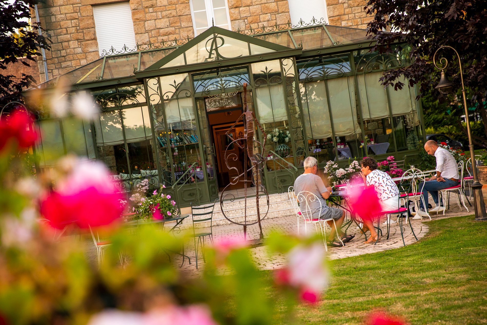 Jardin fleuri de l'Hôtel La Ramade avec personnes floues, symbolisant la beauté naturelle de l'établissement.
