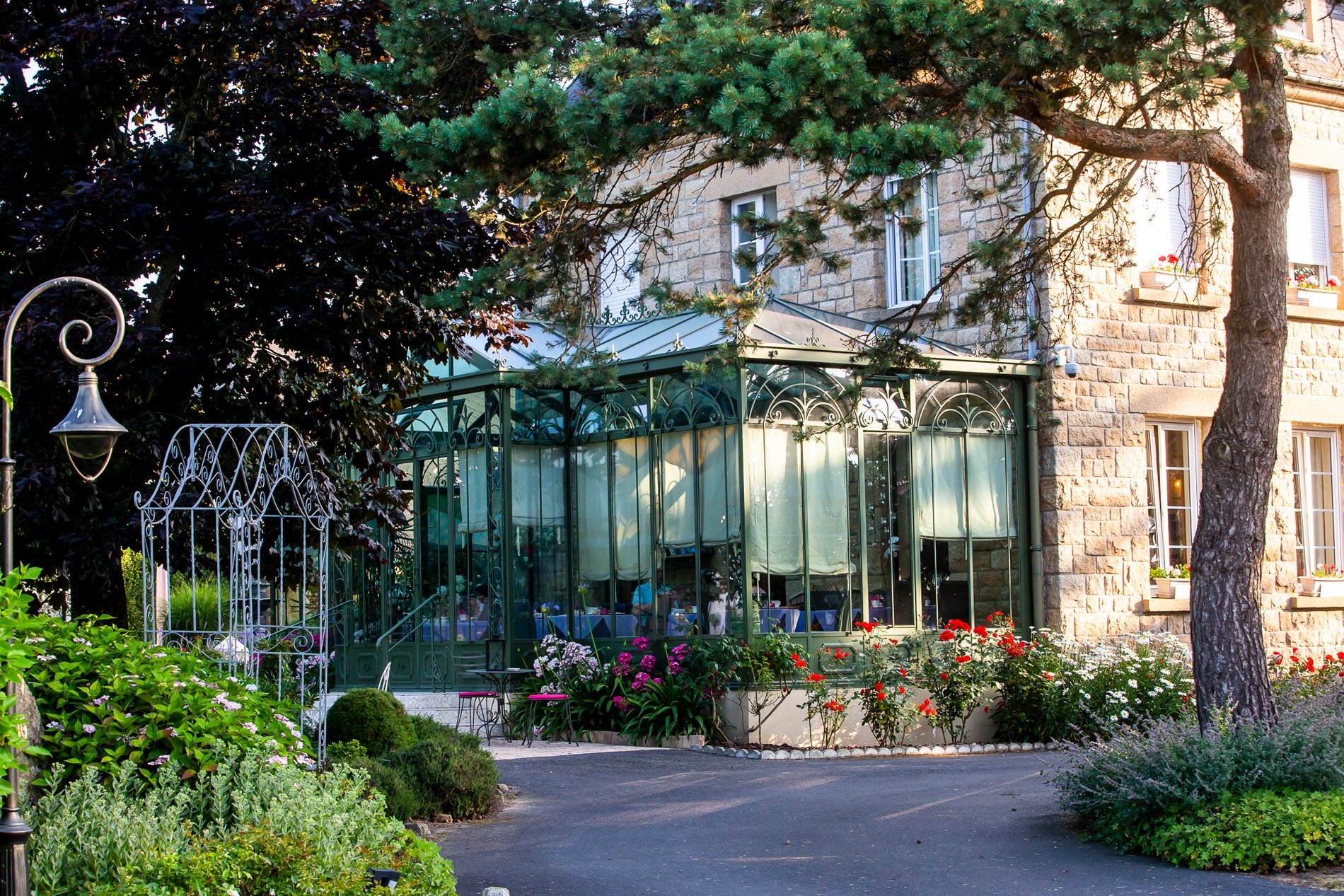 Véranda de l'Hôtel La Ramade vue de l'extérieur avec plantes, symbolisant un espace lumineux et végétalisé.