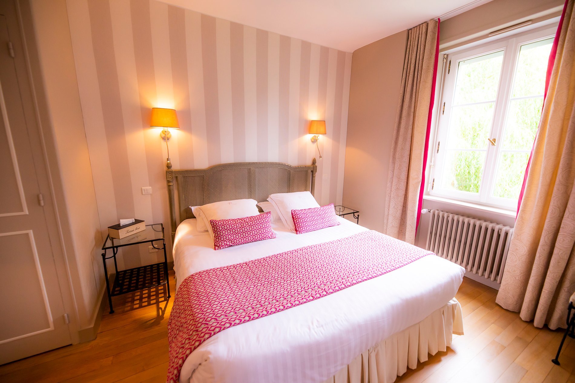 Chambre de l'Hôtel La Ramade avec murs rayés roses et blancs, symbolisant un style classique et coloré.
