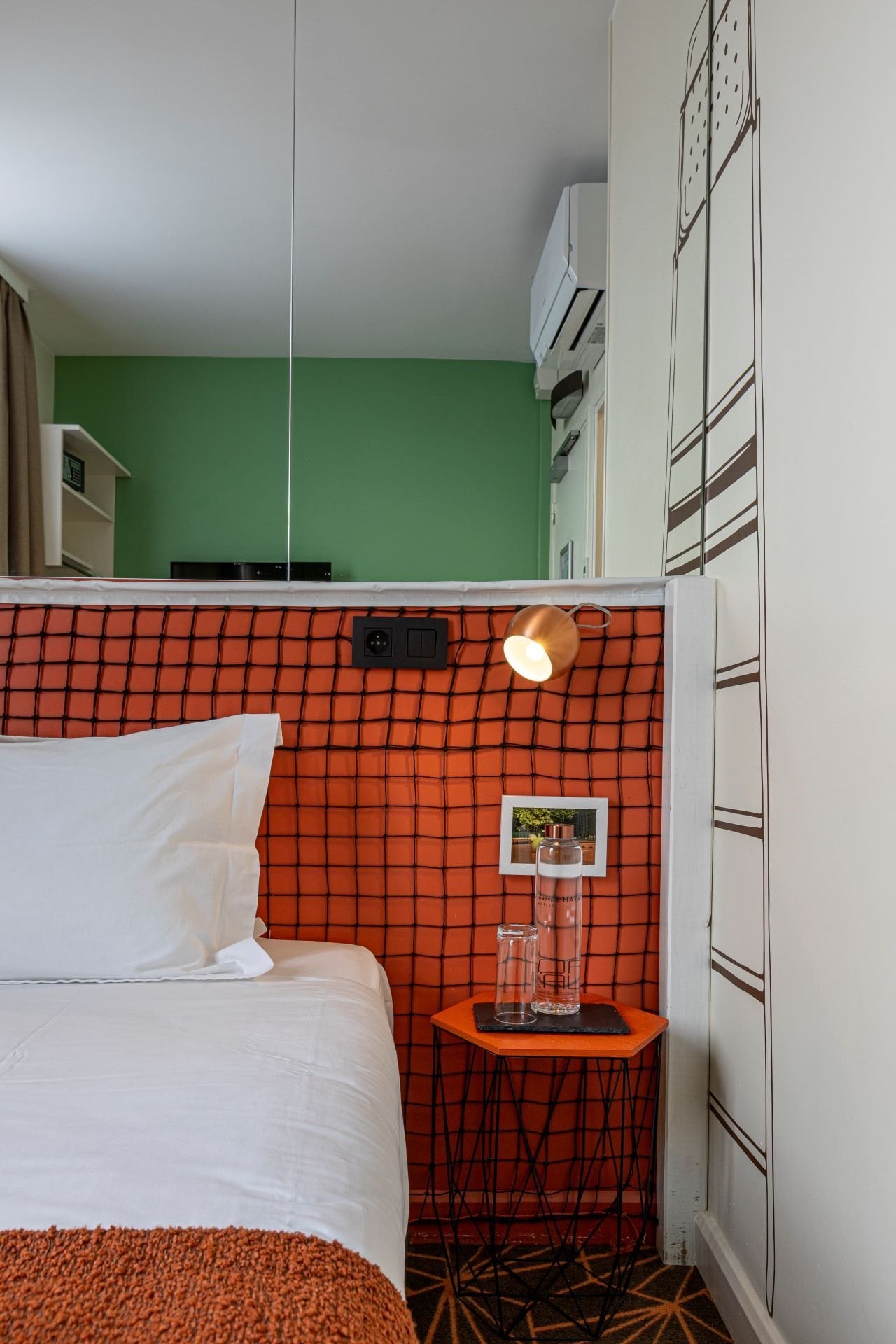 Détail d’une chambre de l’Hôtel Olympic à Boulogne-Billancourt avec tête de lit inspirée du tennis, éclairage de lecture et équipements de confort.