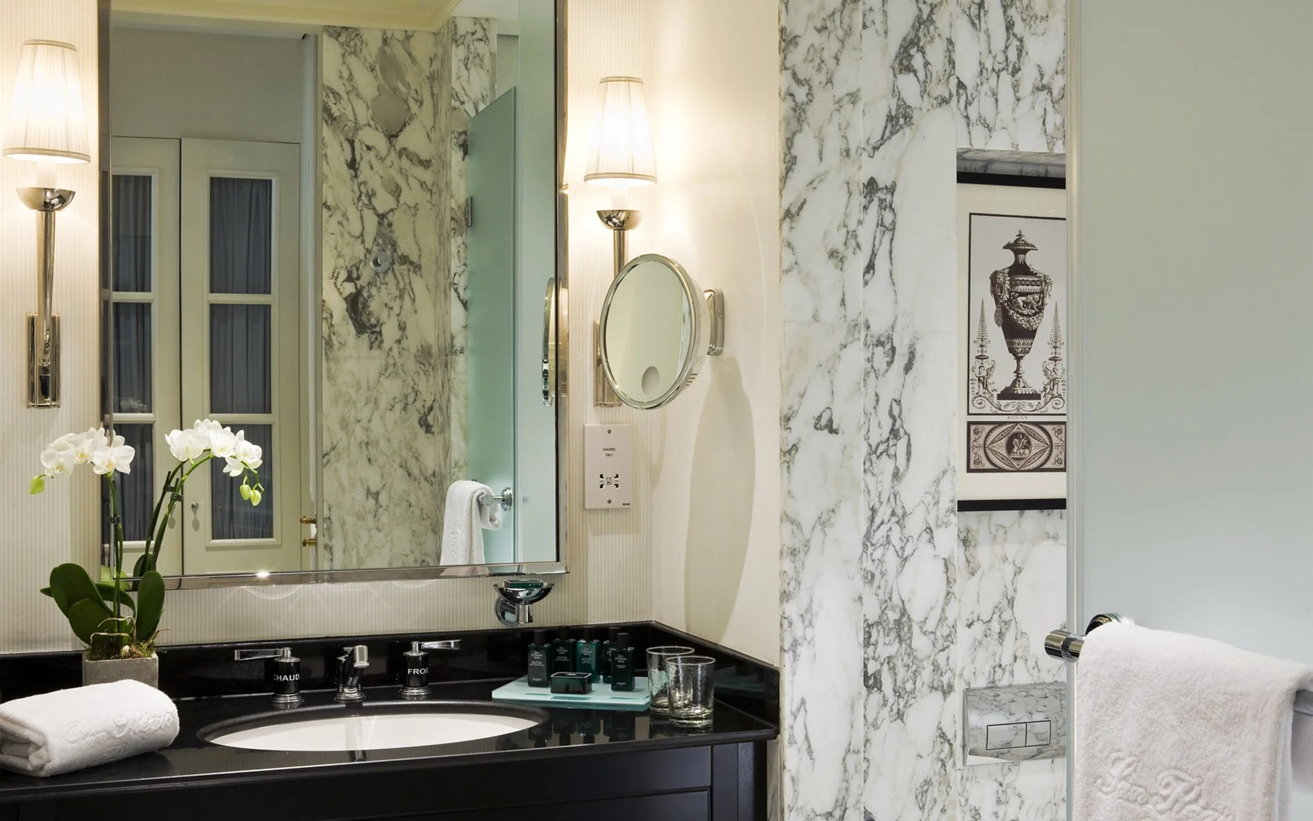 Salle de bain en marbre à l’Hôtel San Régis, avec vasque noire, orchidée blanche et produits d’accueil de luxe.